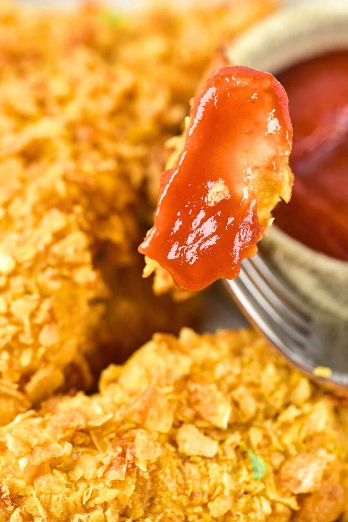 Fork holding up cornflake chicken dipped in ketchup
