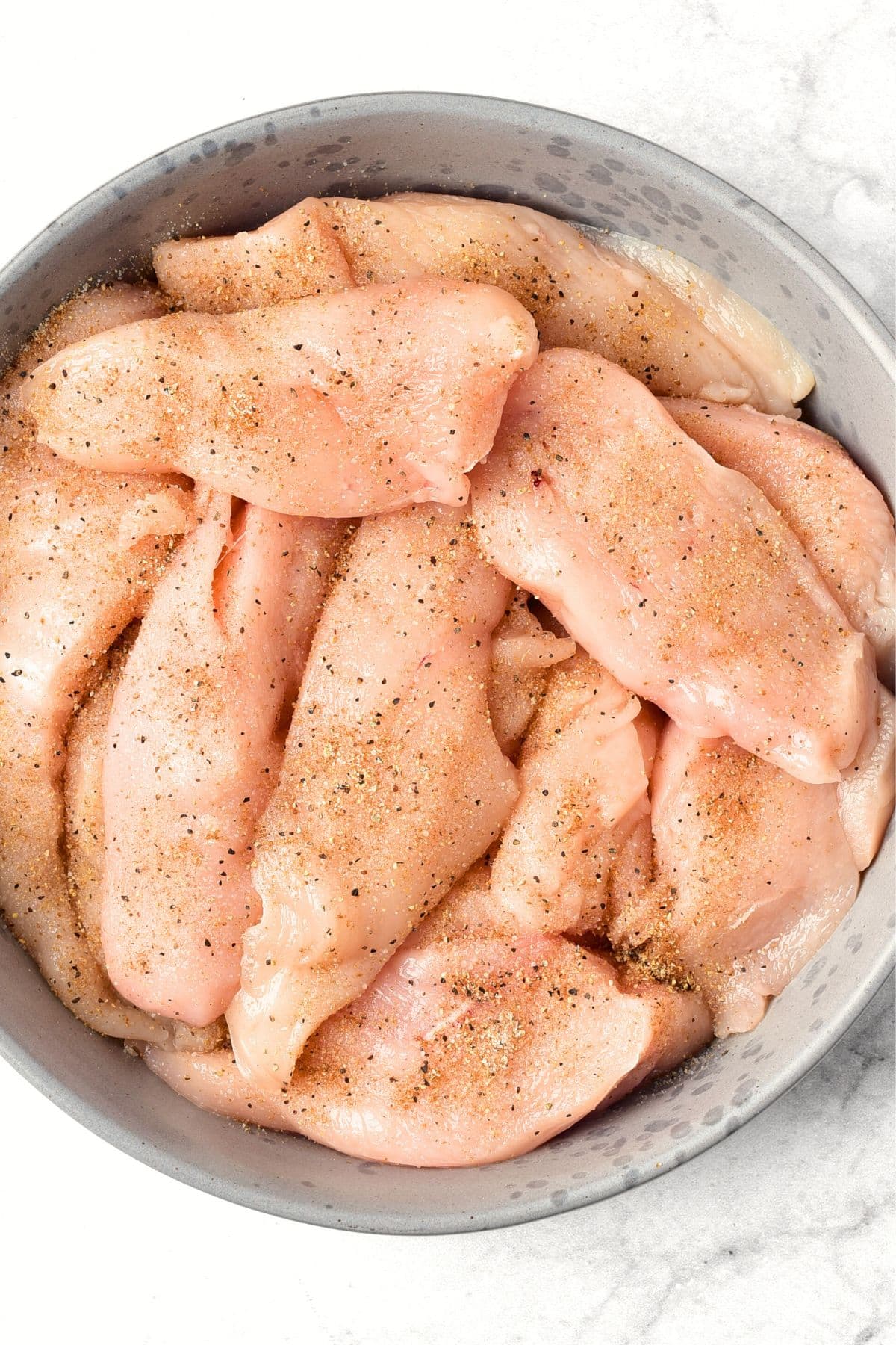 Raw chicken strips sprinkled with ground pepper and spices.