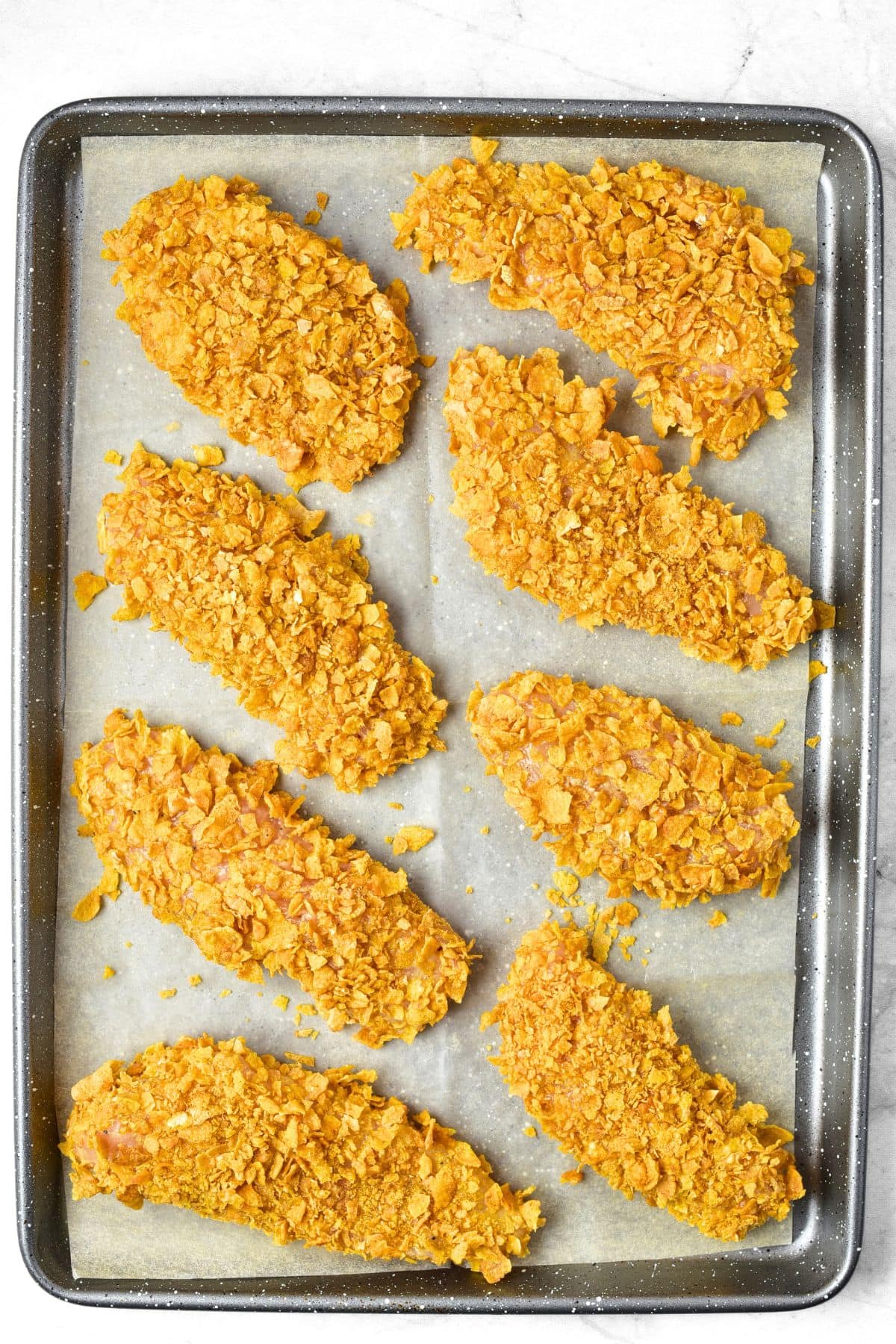 Cornflake chicken on parchment-lined baking sheet