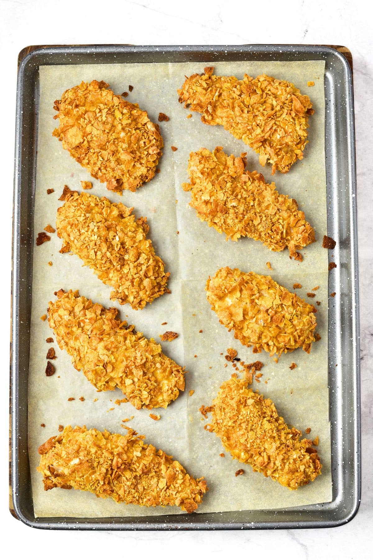Cornflake chicken on parchment-lined baking sheet