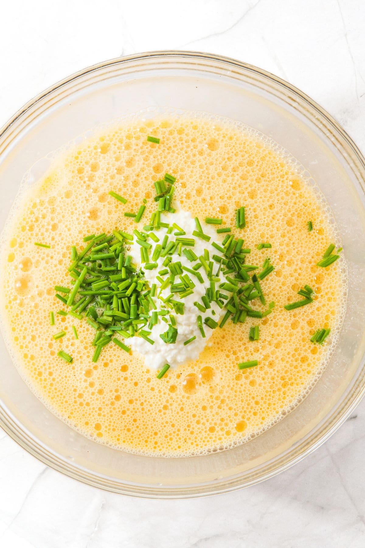 Chopped fresh chives and cottage cheese on top of pale yellow liquid mixture.