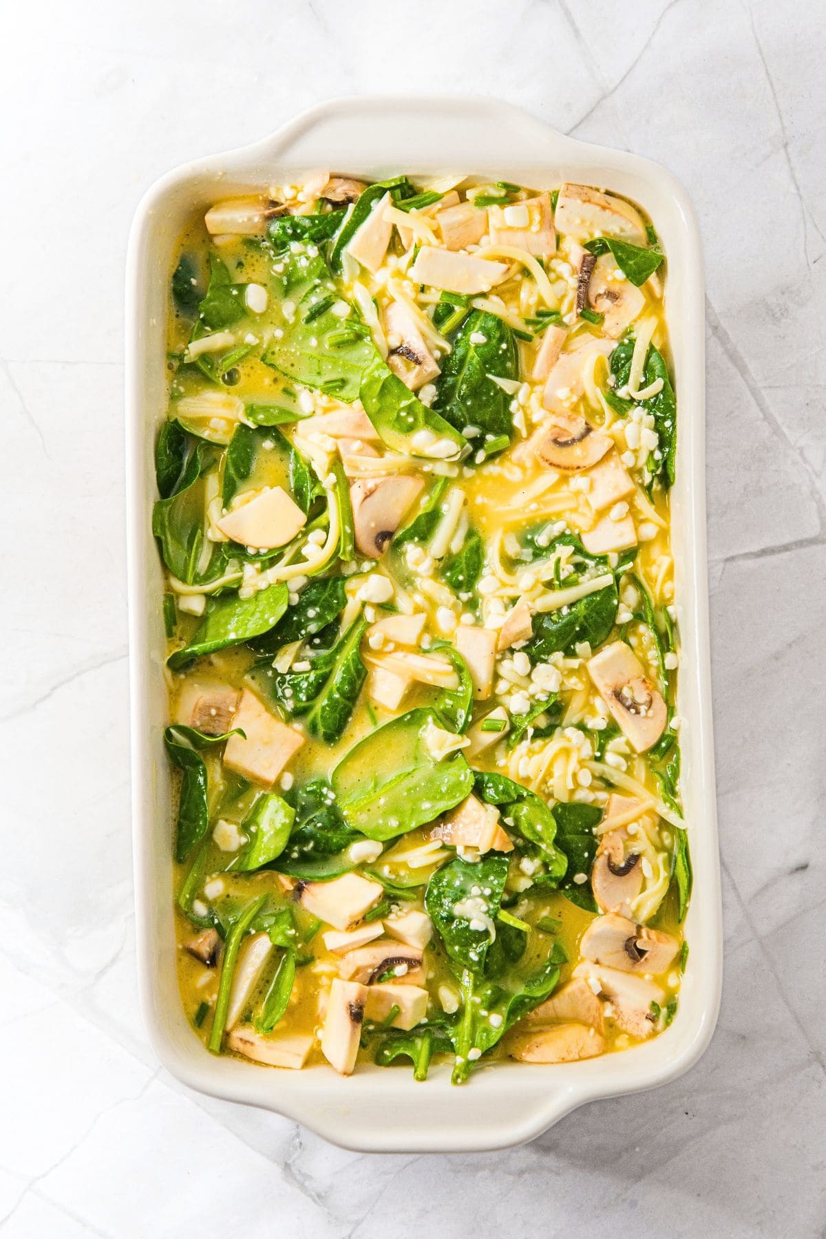 Spinach, mushrooms, cottage cheese and egg mixture in casserole dish.