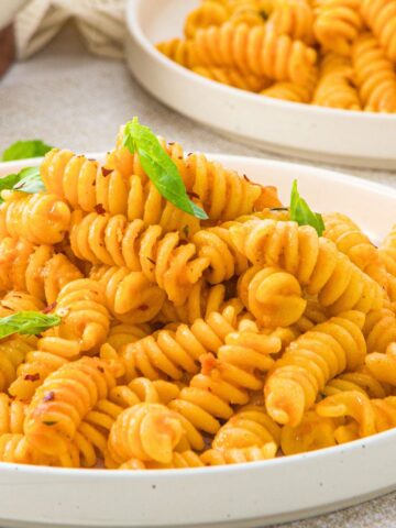 A plate of fusilli pasta garnished with basil leaves