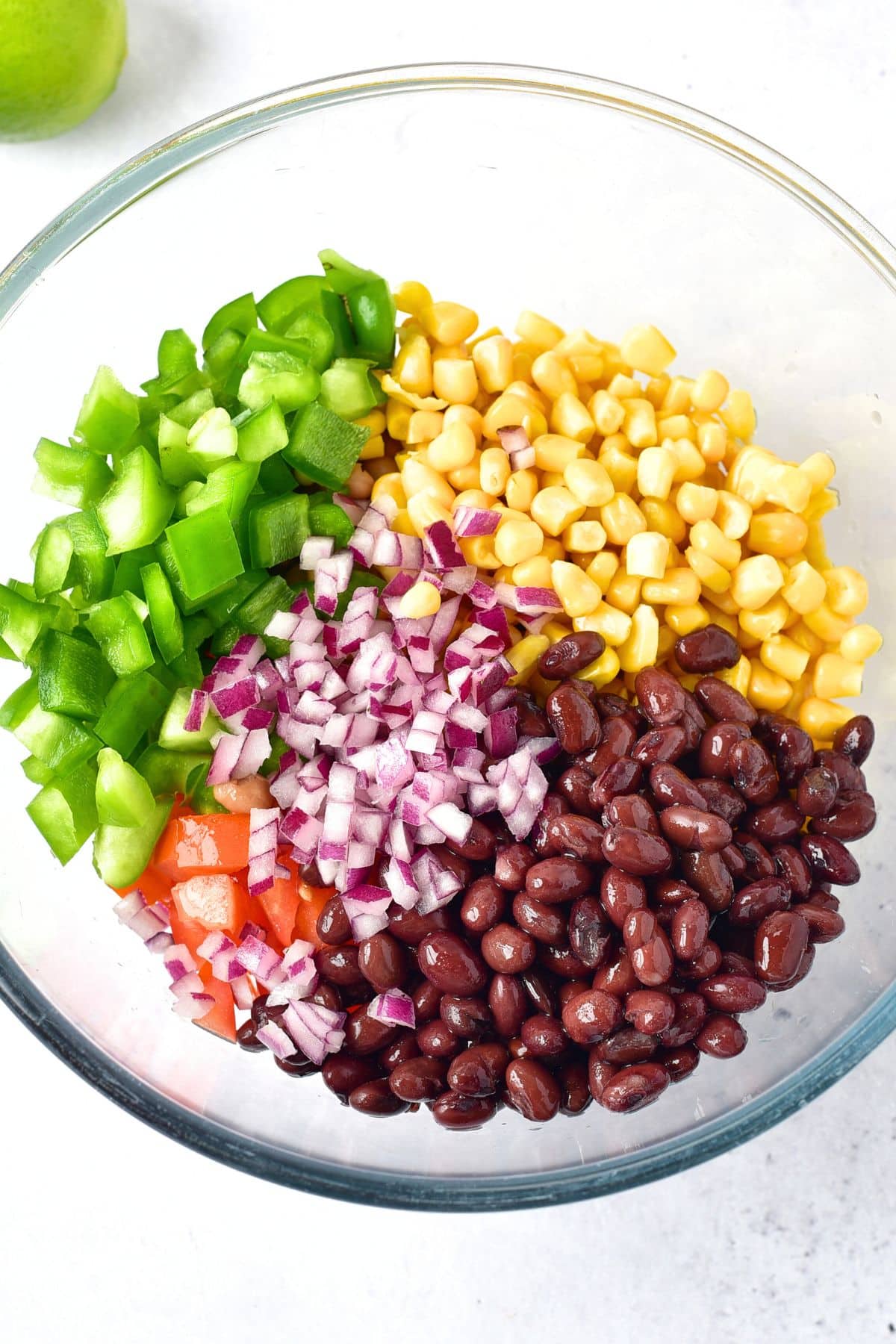 Black beans, diced bell peppers, corn kernels, diced red onions in glass bowl.