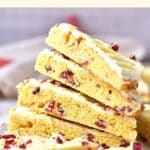 A stack of gluten-free cranberry bliss bars on wooden board.