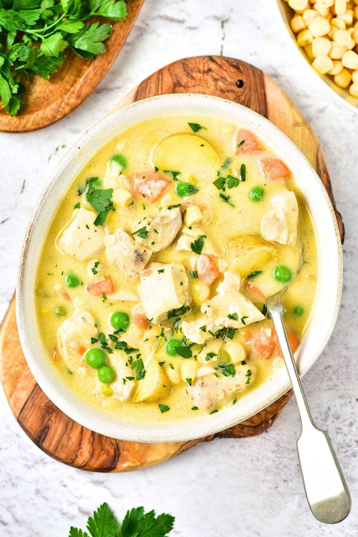 Top down view of a bowl of creamy chicken soup on wooden board.