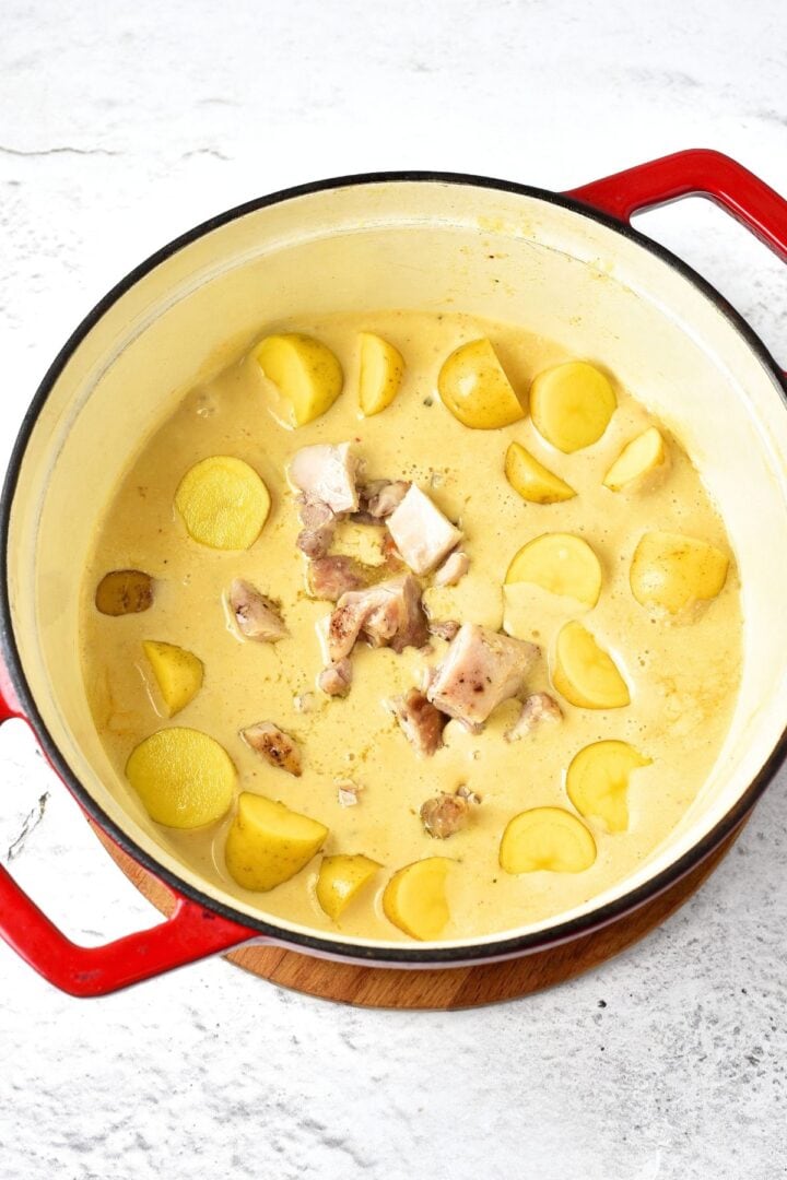 A pot of halved baby potatoes and chicken pieces in creamy broth.
