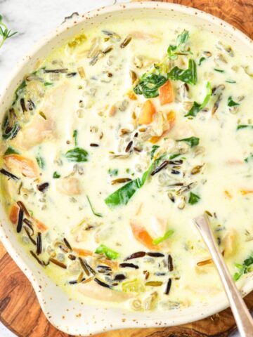 A bowl of chicken and wild rice soup on wooden board.