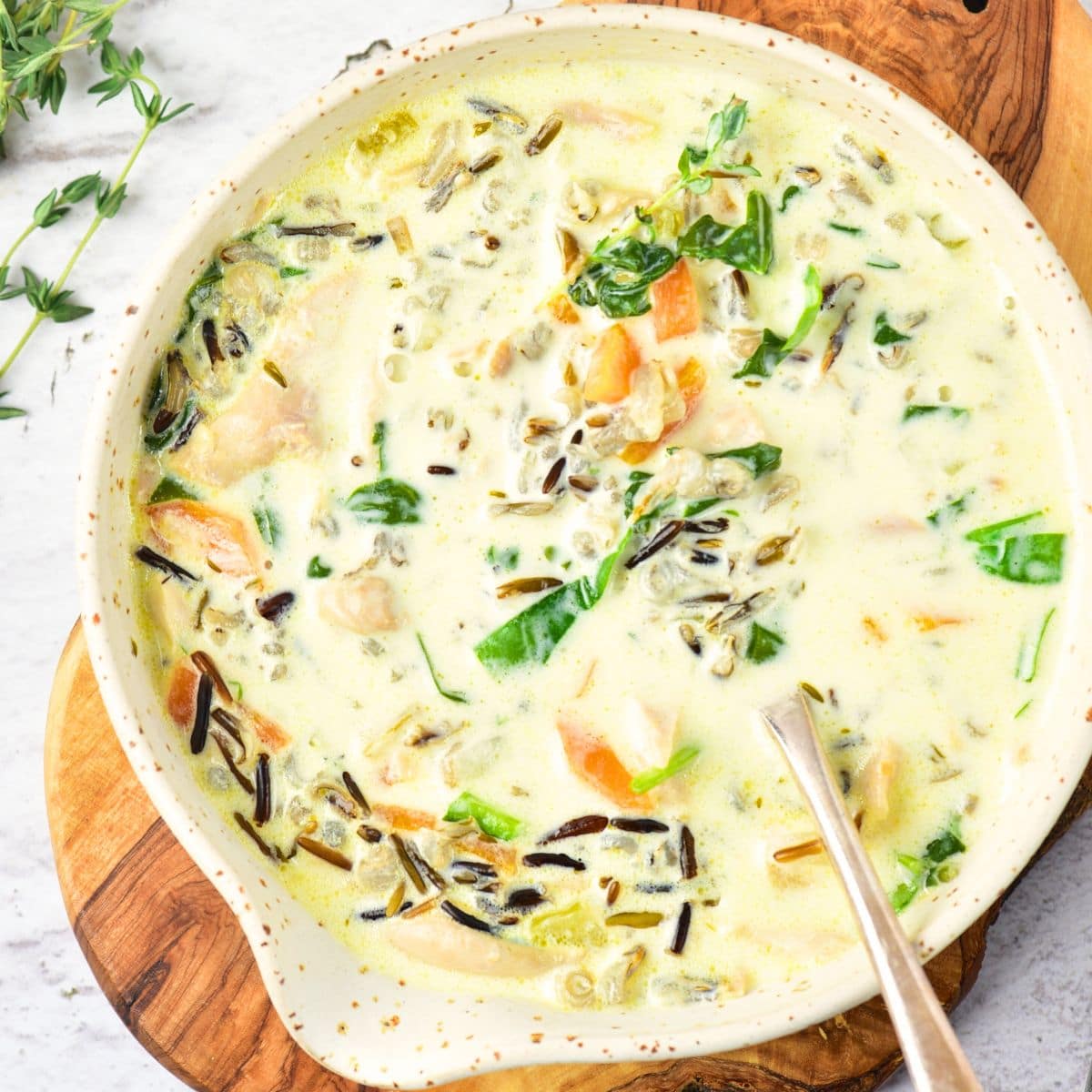 A bowl of chicken and wild rice soup on wooden board.