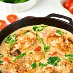 Cast iron skillet with Tuscan chicken on wooden board.