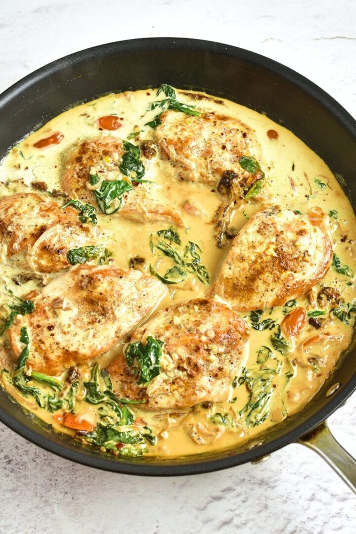 Cooked chicken breasts in creamy sauce with spinach in skillet
