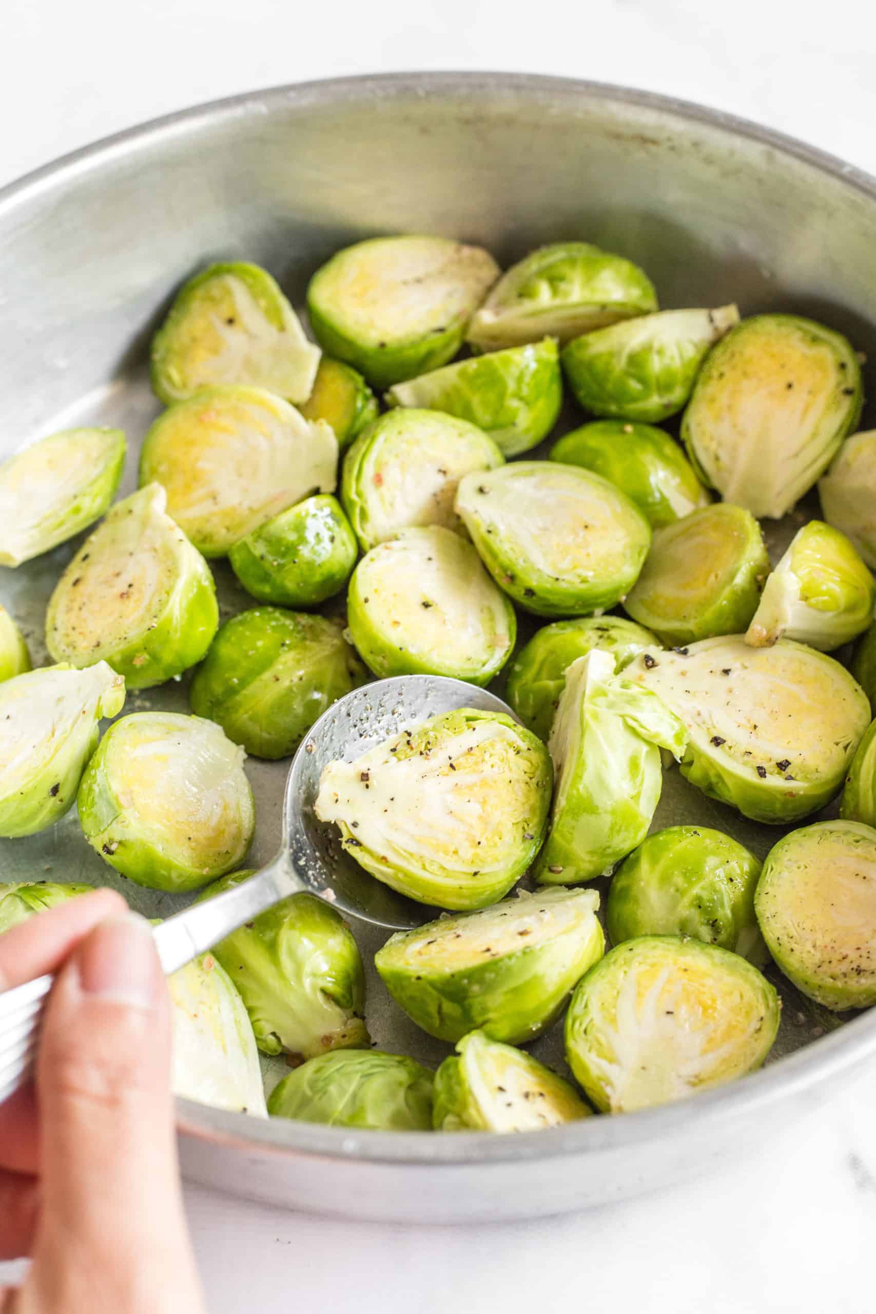 Tossing Brussels sprouts together with oil, salt and pepper in a mixing bowl.