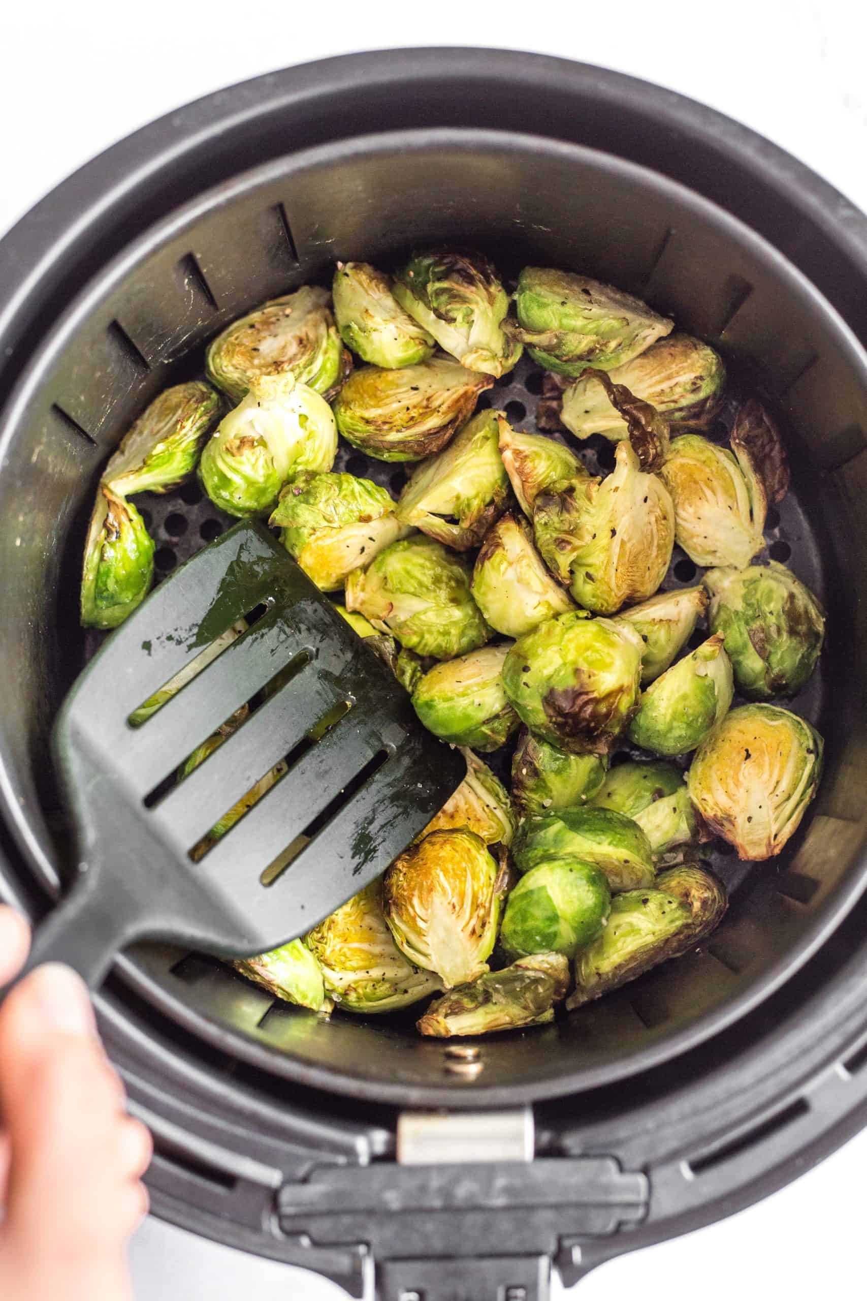 Using a spatula to toss air fryer Brussels sprouts in the air fryer basket.