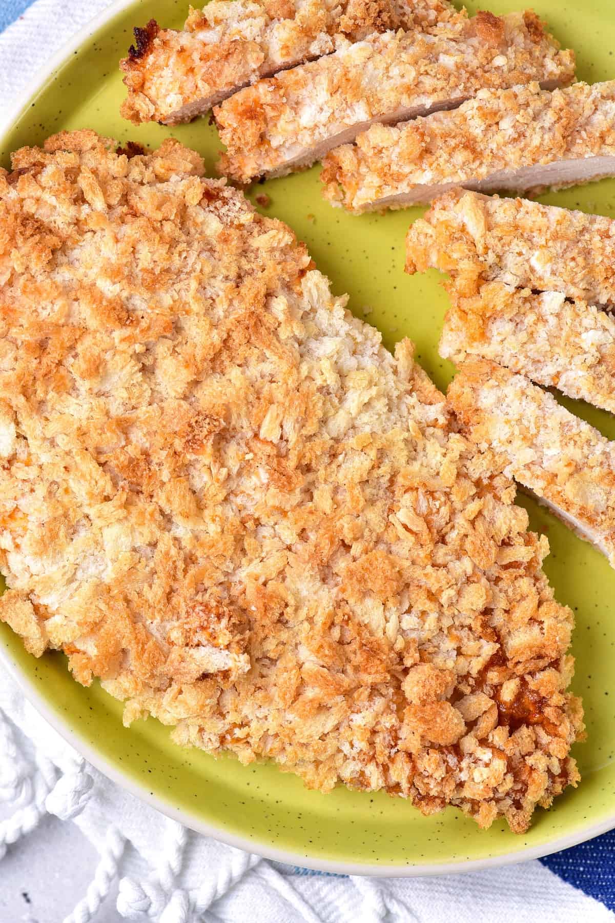 Sliced pieces of breaded chicken breast on green plate.