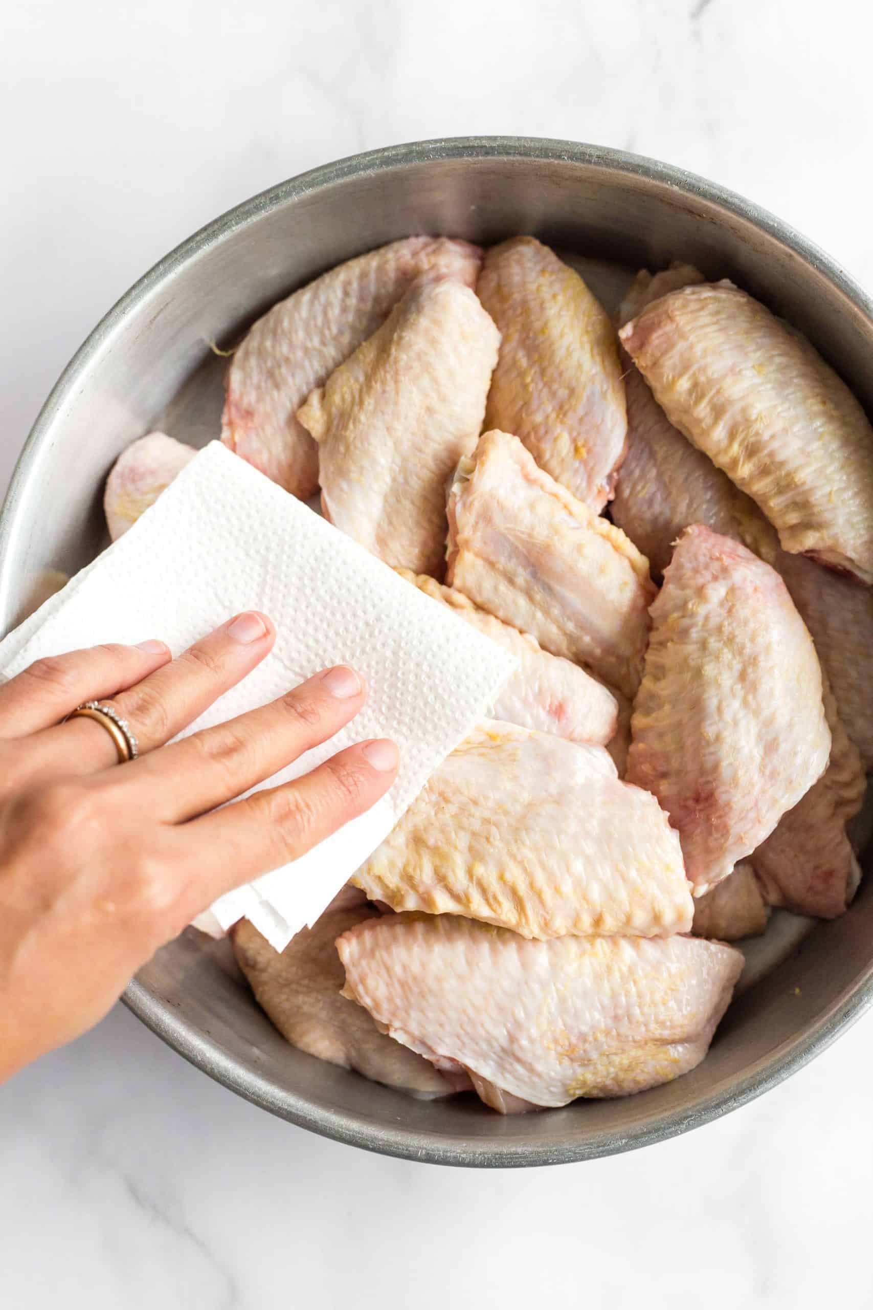 A hand patting the chicken wings dry with a paper towel.