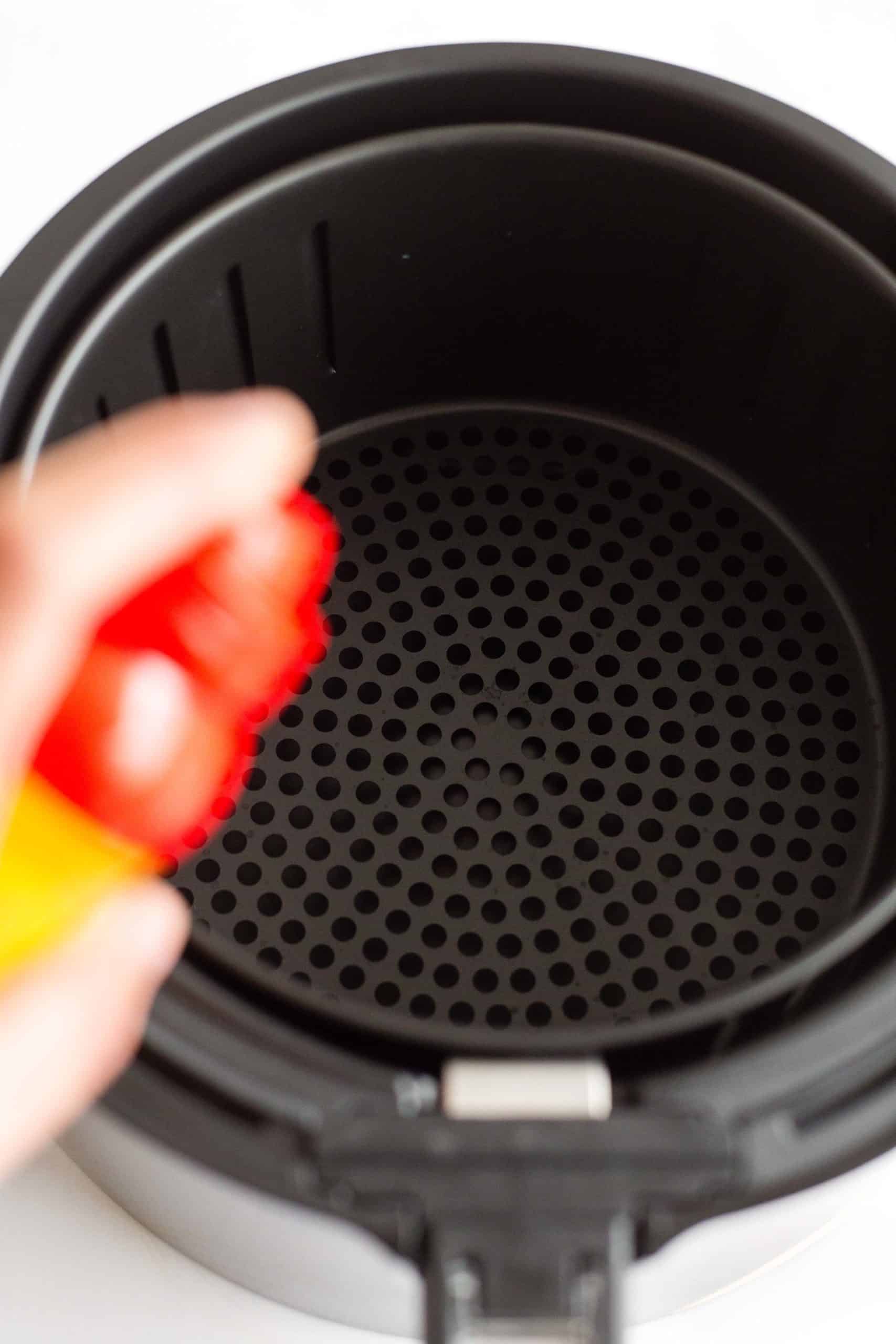 Spraying the air fryer basket with non-stick cooking spray.