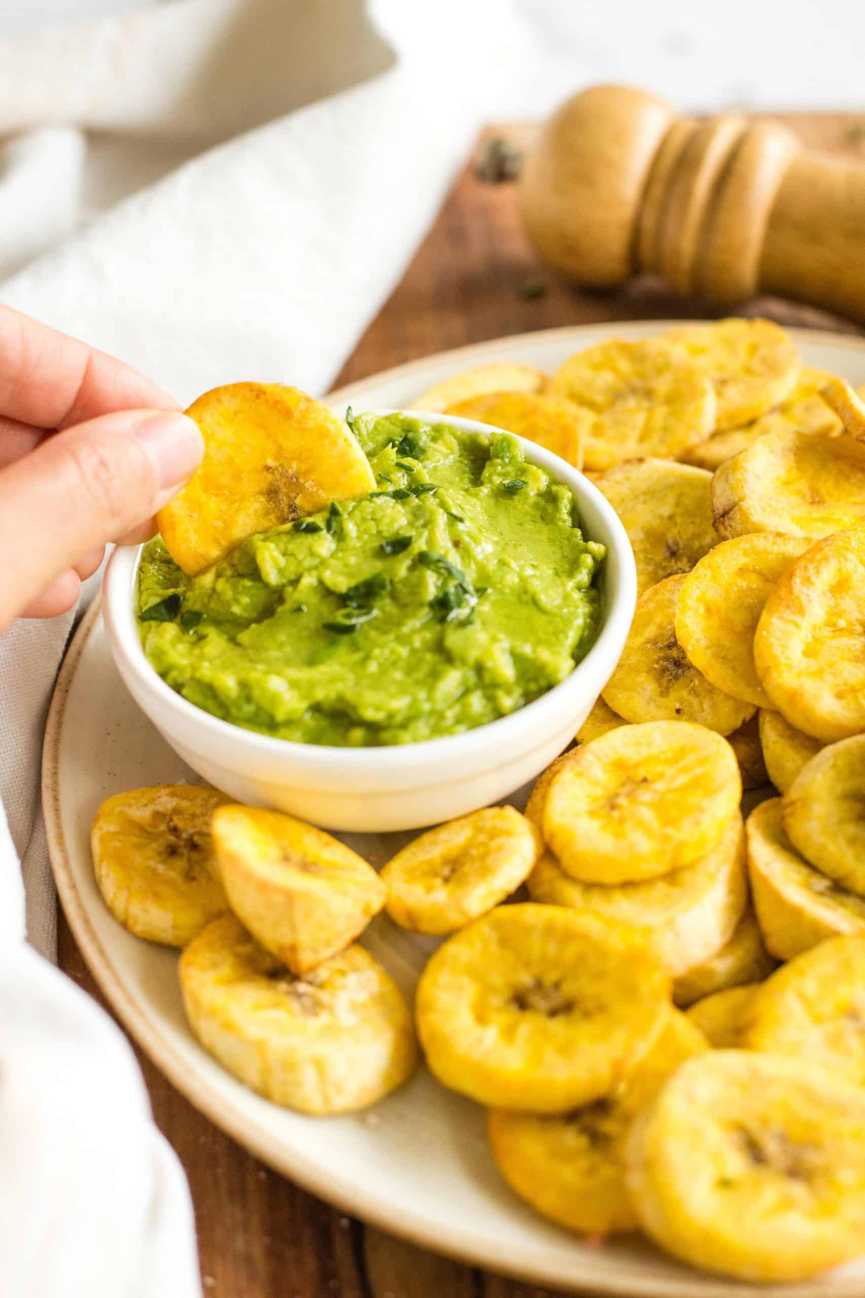 Dipping an air fryer plantain chip into a bowl of guacamole.