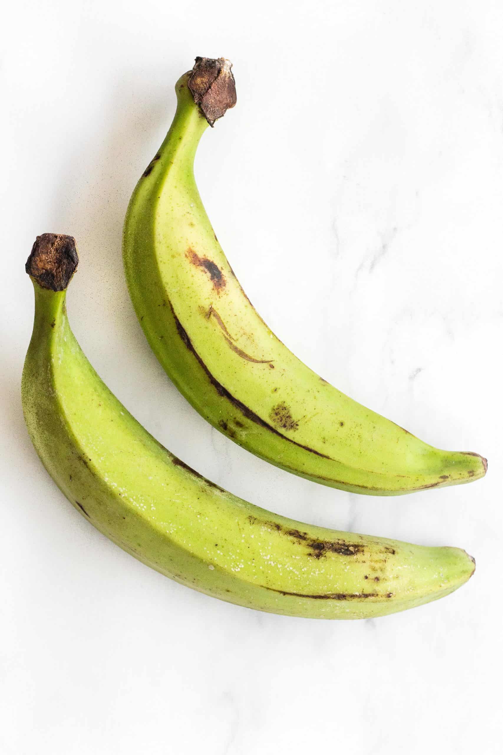 Green unripened plantains on a marble board.