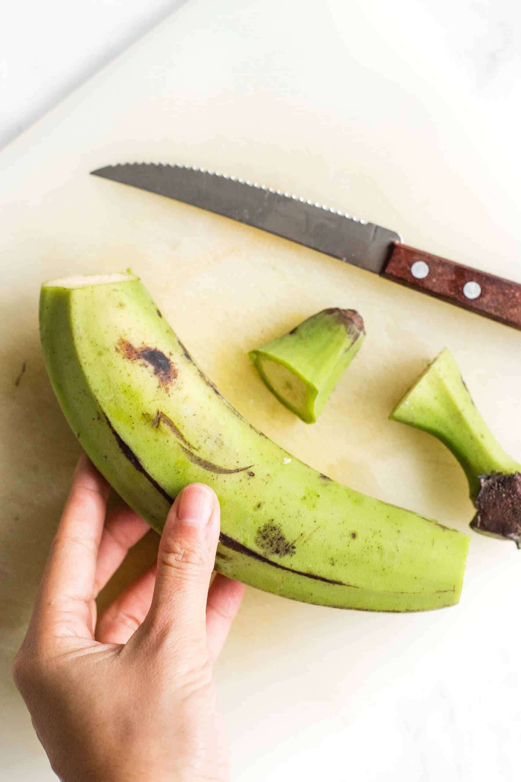 Holding a green plantain with its ends cut off.