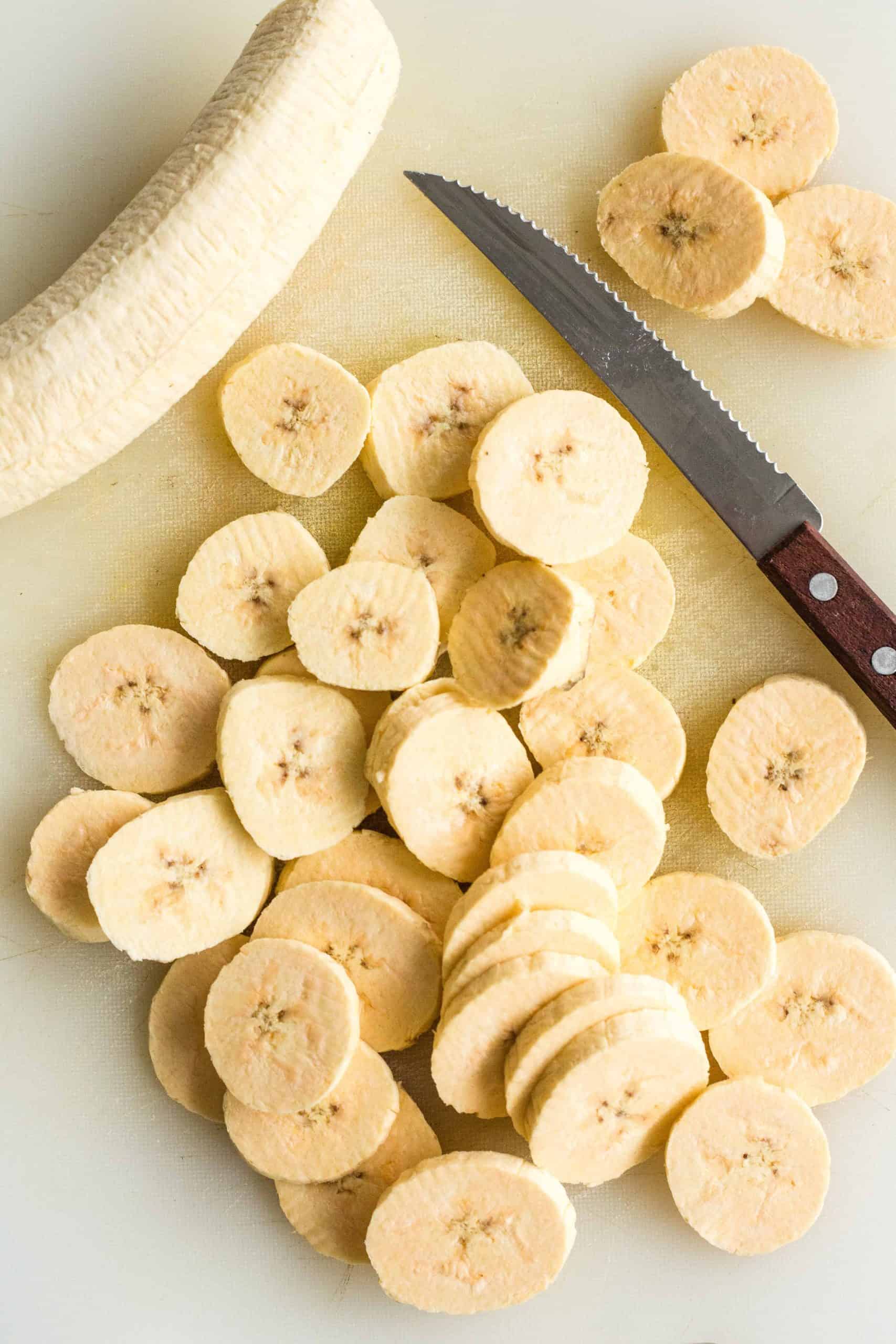 Sliced plantains and a knife on a chopping board.