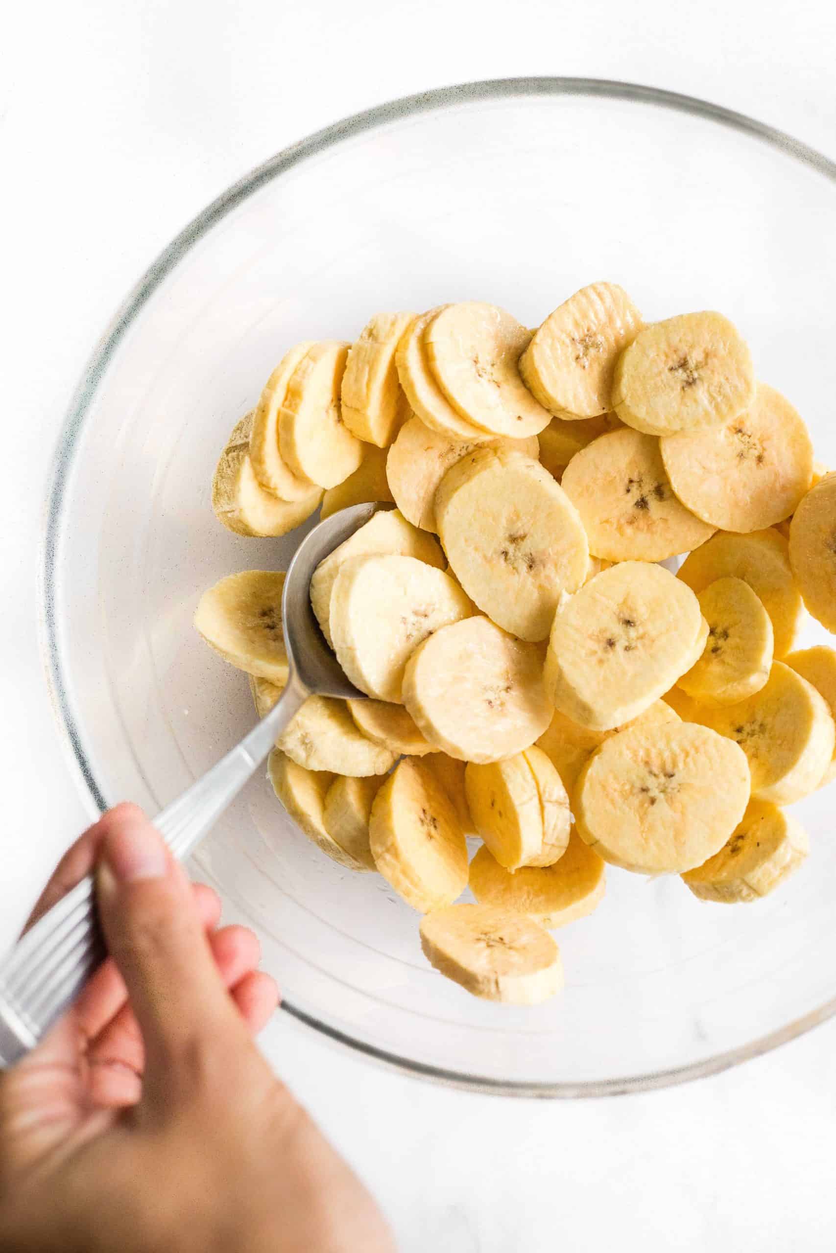 Tossing sliced plantains with oil in a large mixing bowl.