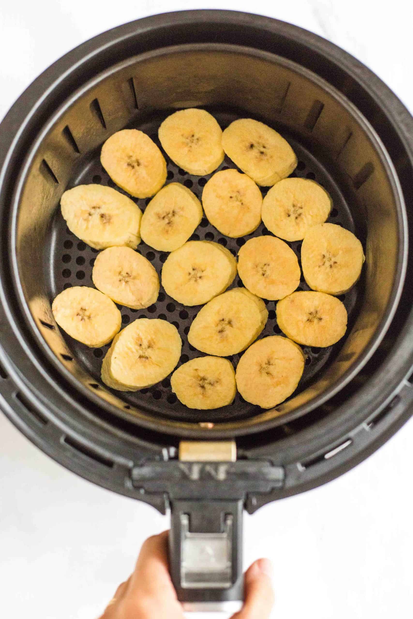 Sliced plantains in a single layer in air fryer basket.