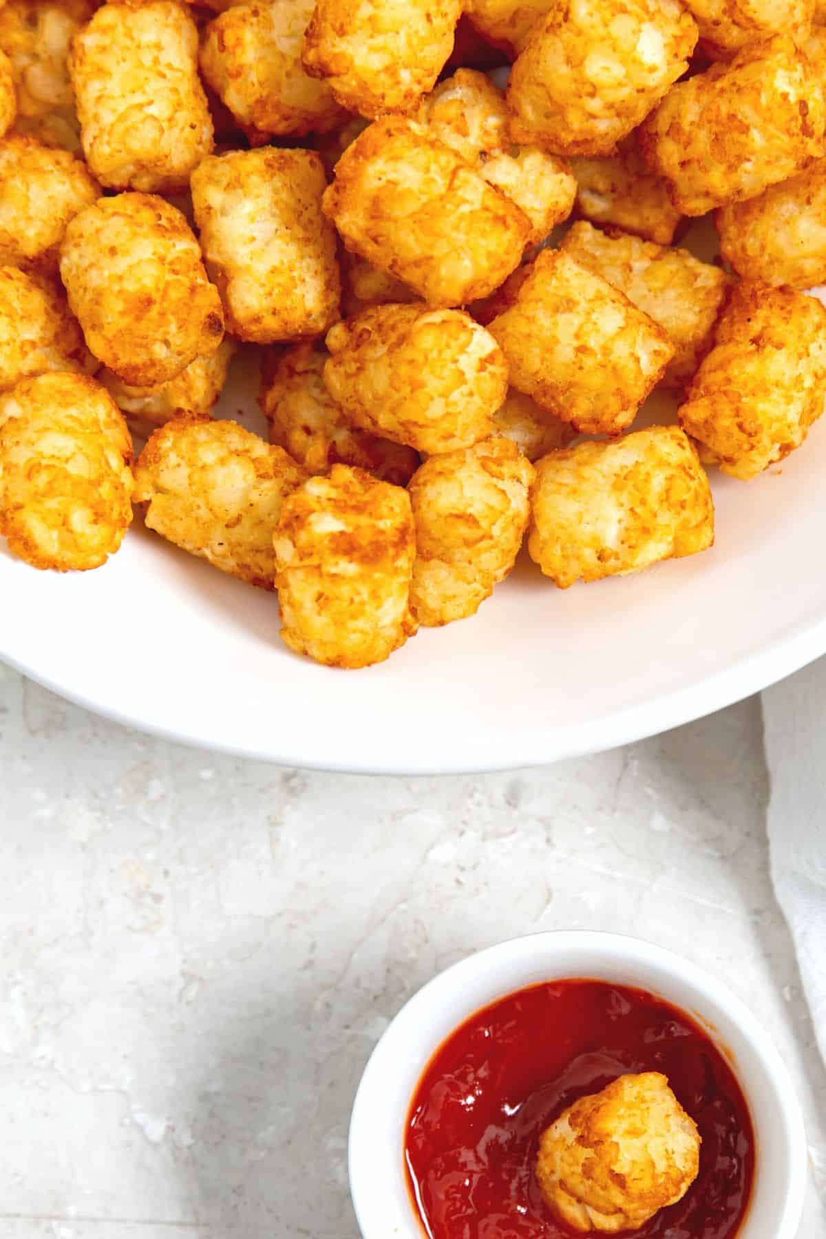Top down view of a bowl of air fried tater tots and a small ramekin with ketchup.