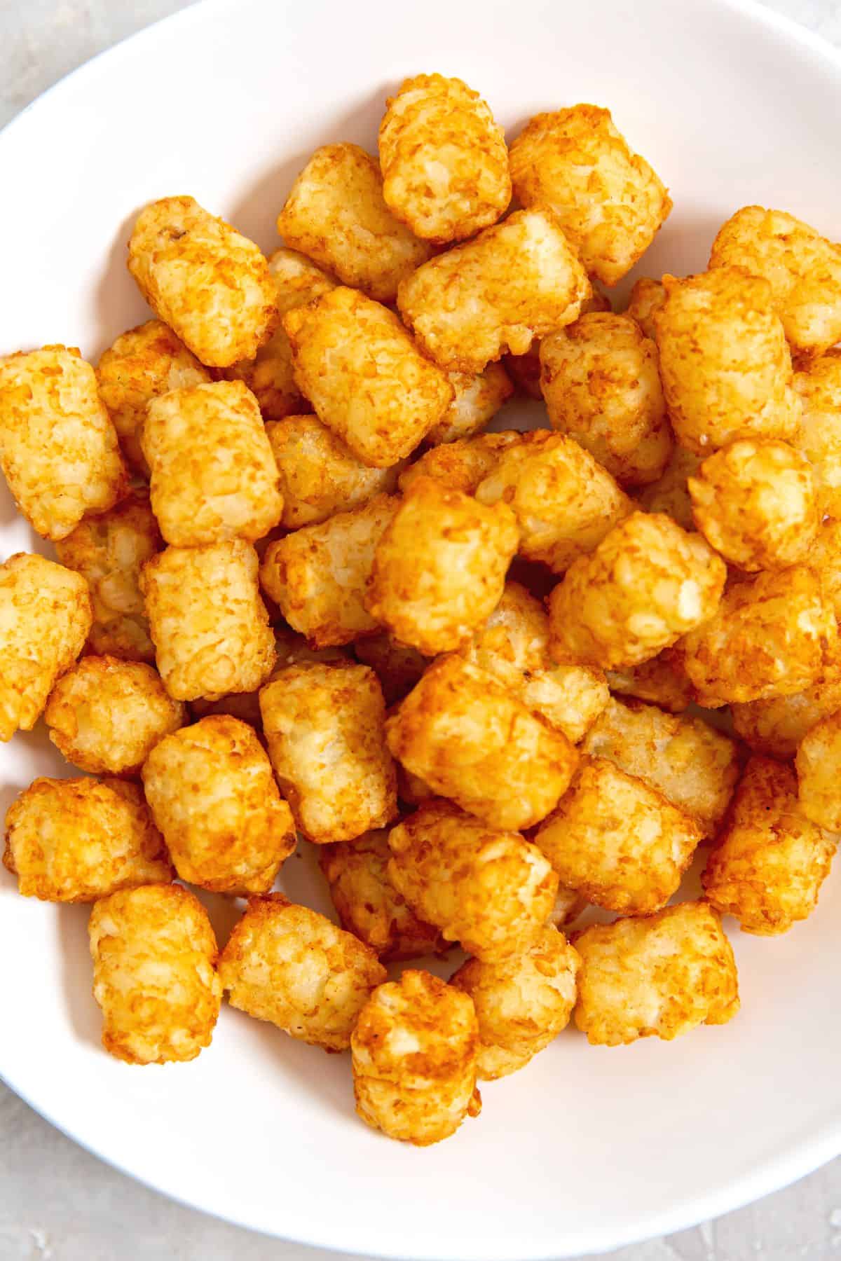Freshly cooked air fryer tater tots in a white bowl.