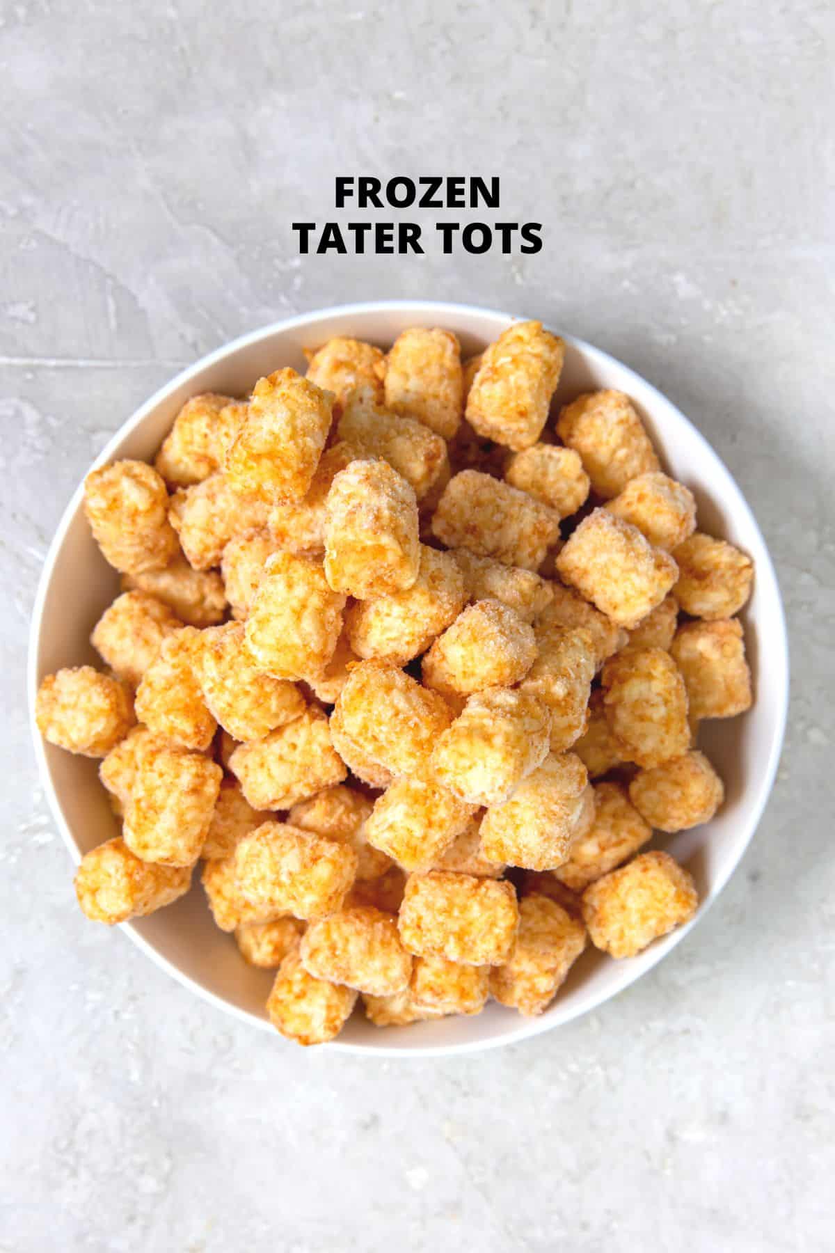 A bowl of frozen tater tots on a grey background.