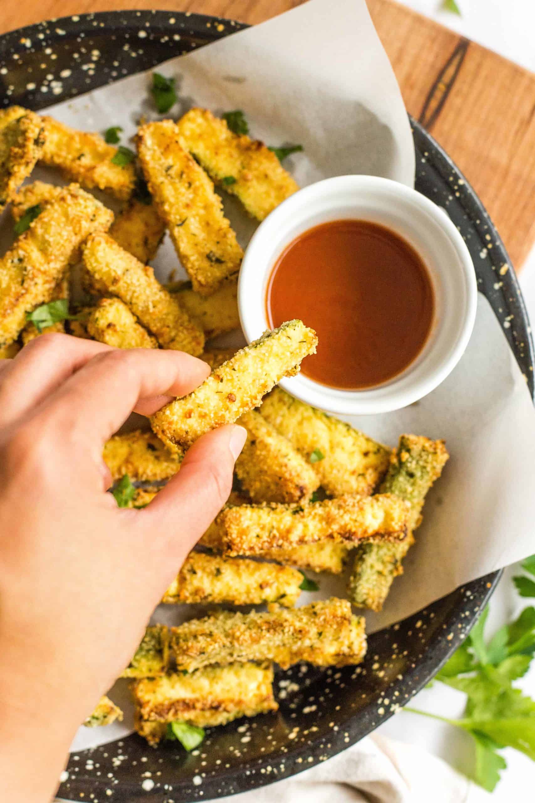 Hand holding up a freshly cooked zucchini fry.