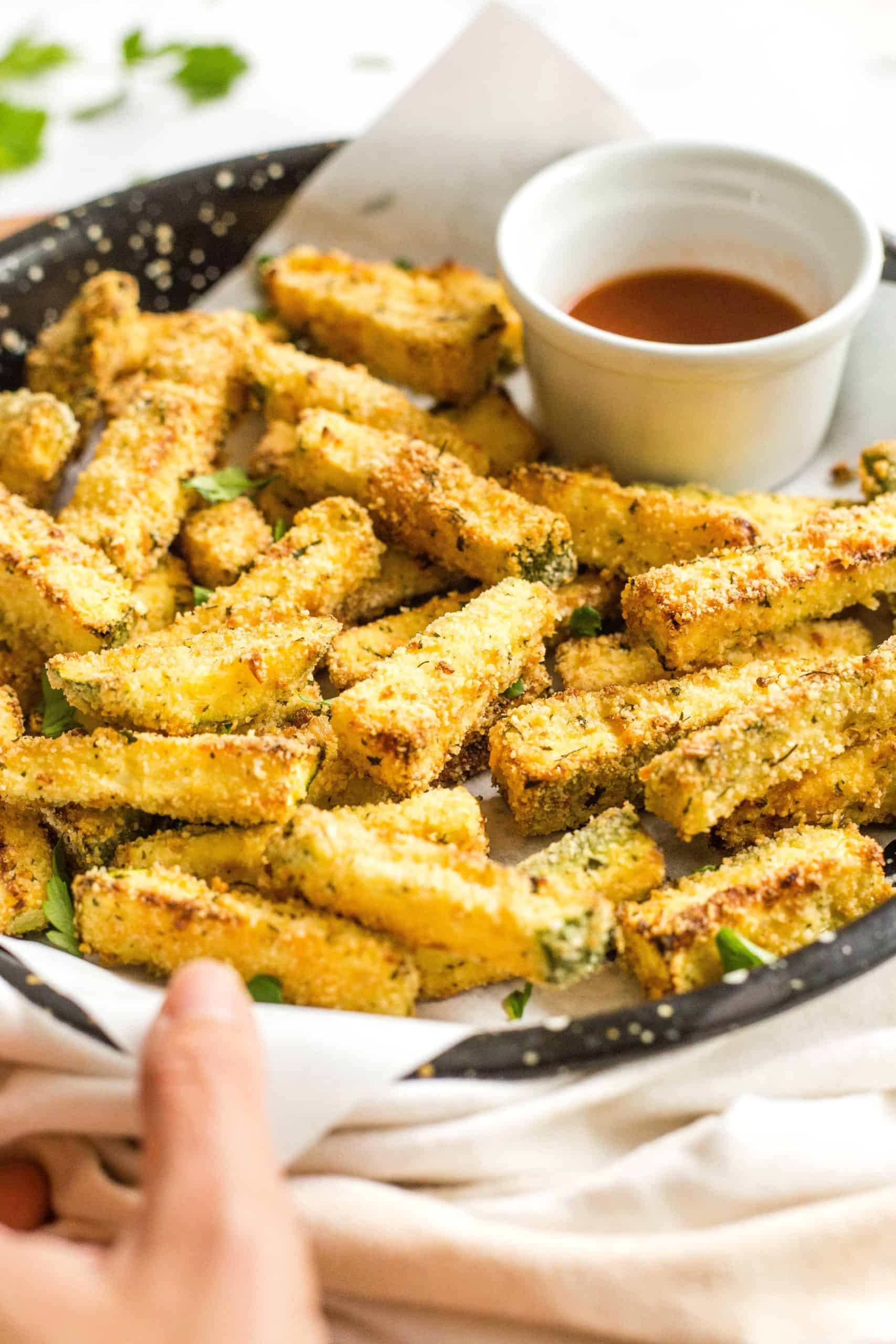 Hand holding a baking sheet of freshly cooked air fryer zucchini fries.