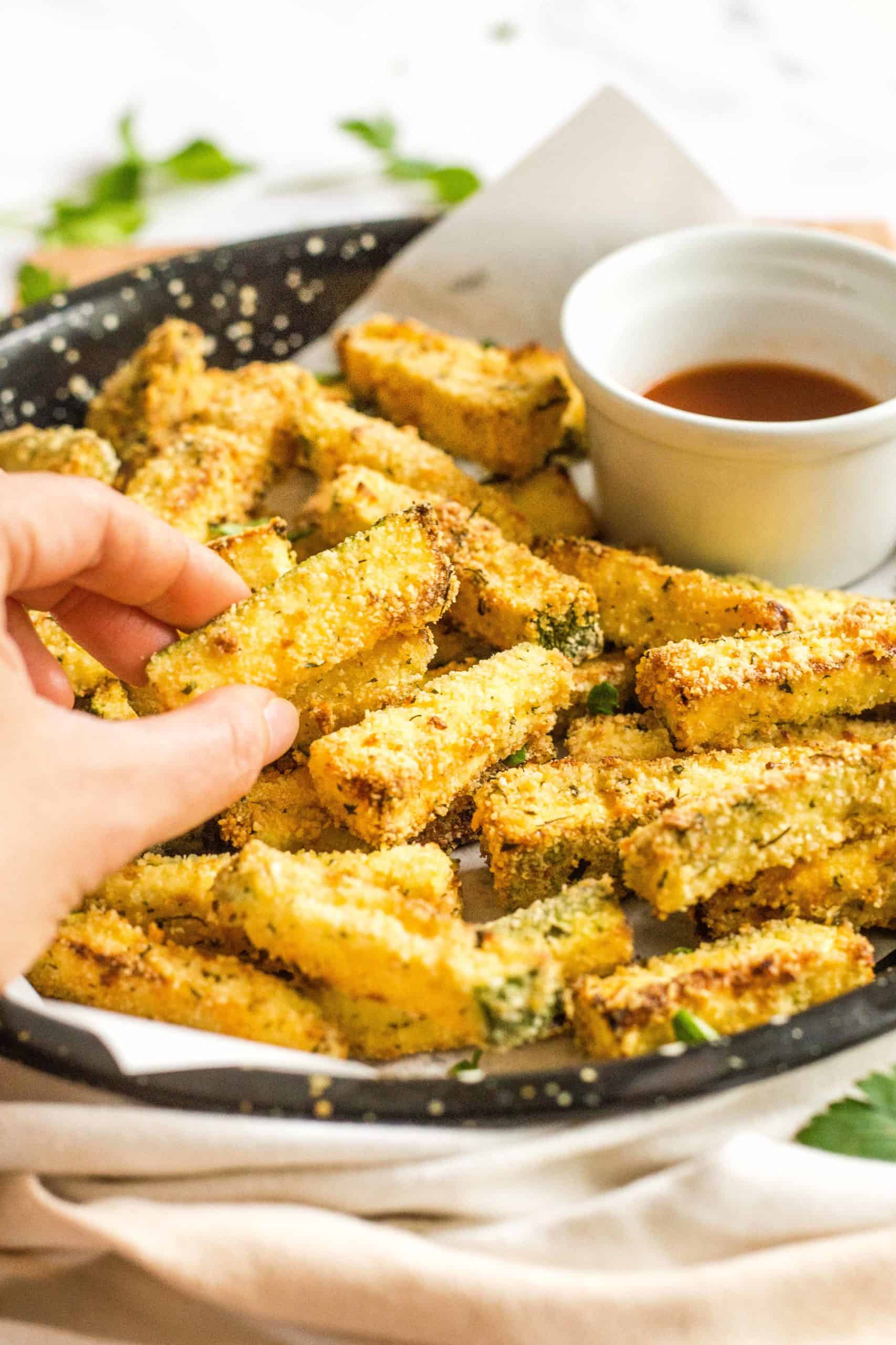 Hand holding up a crispy air fryer zucchini fry.