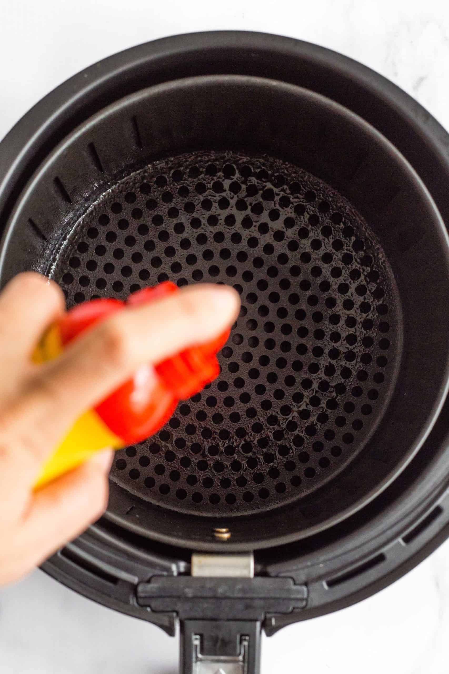 Spraying the air fryer basket with cooking oil.