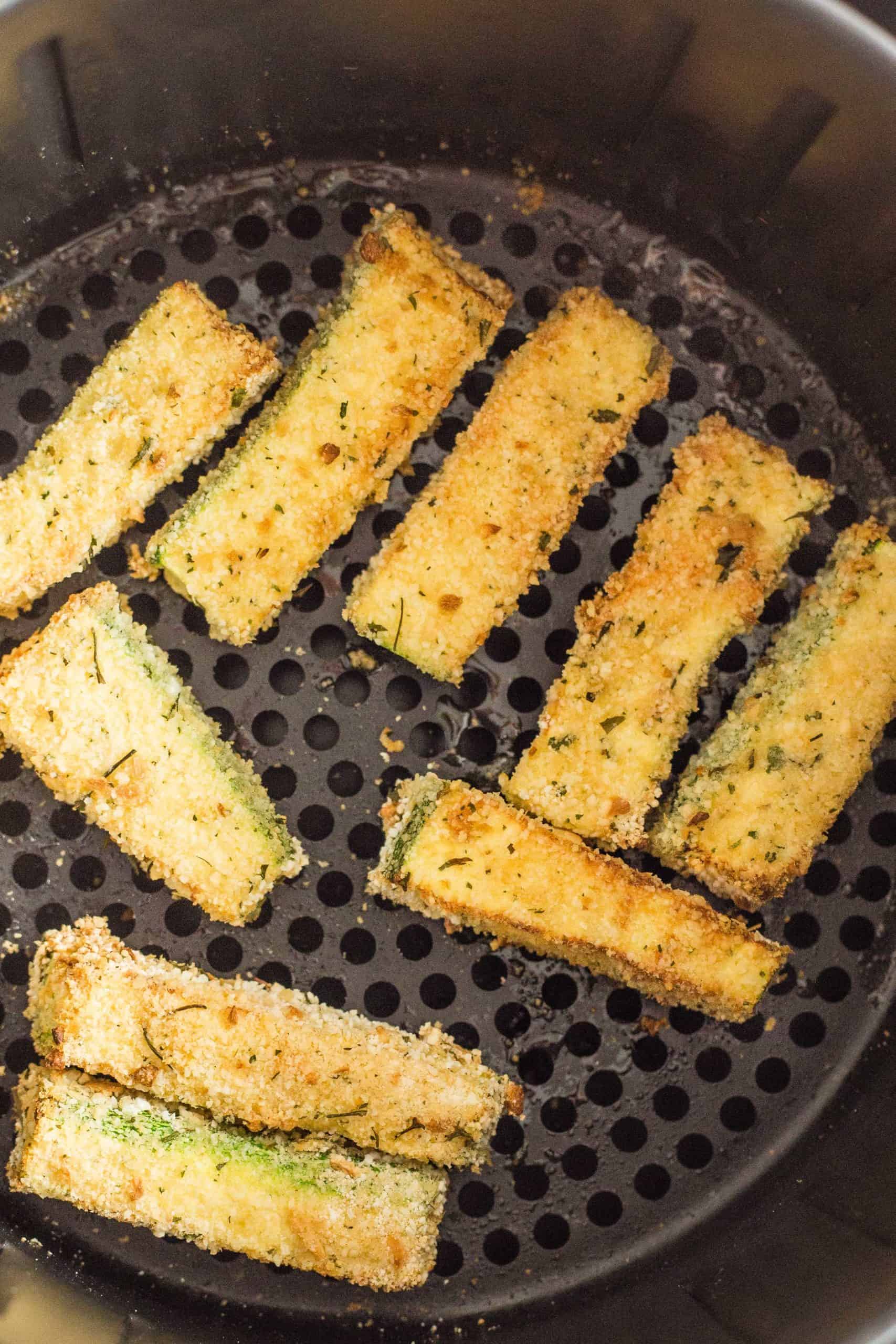 Freshly cooked zucchini fries in an air fryer basket.