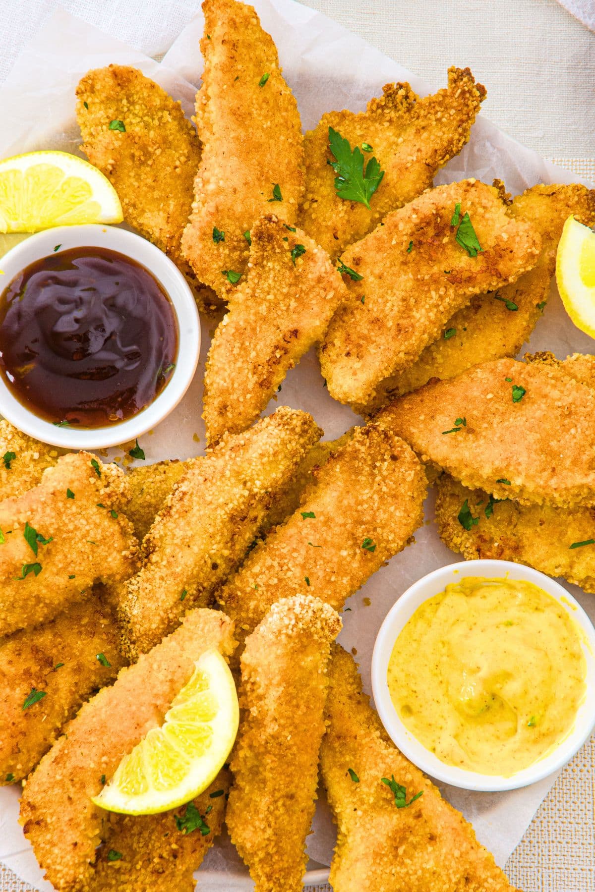 Top down view of crispy baked chicken tenders with mustard and BBQ sauce