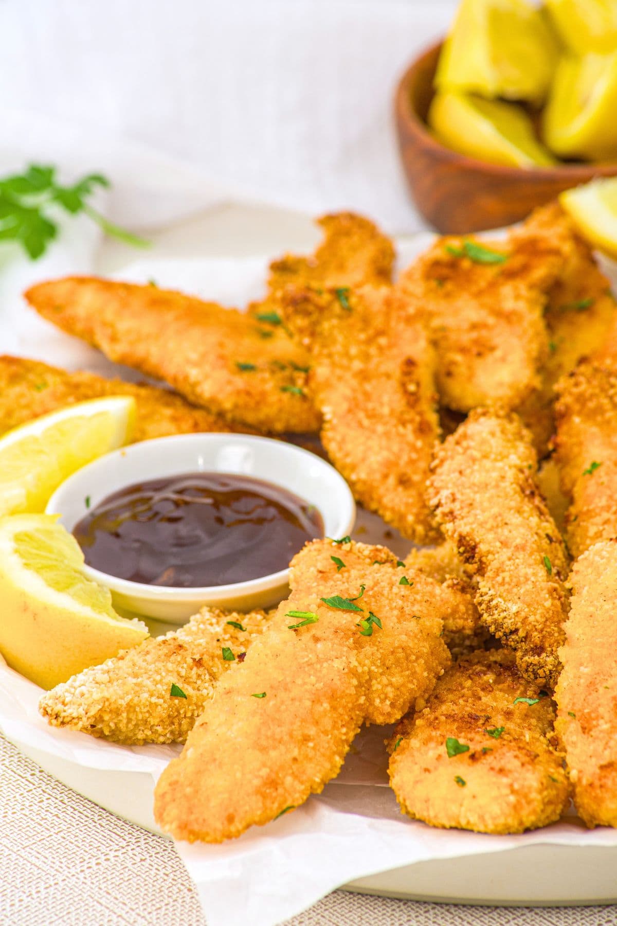 Up close view of a plate of baked chicken tenders with BBQ sauce and lemon wedges