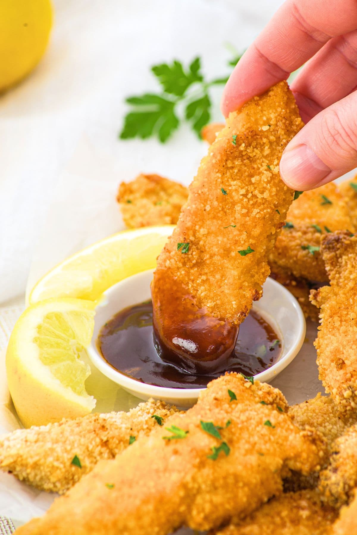 Dipping a baked crunchy chicken tender into BBQ sauce