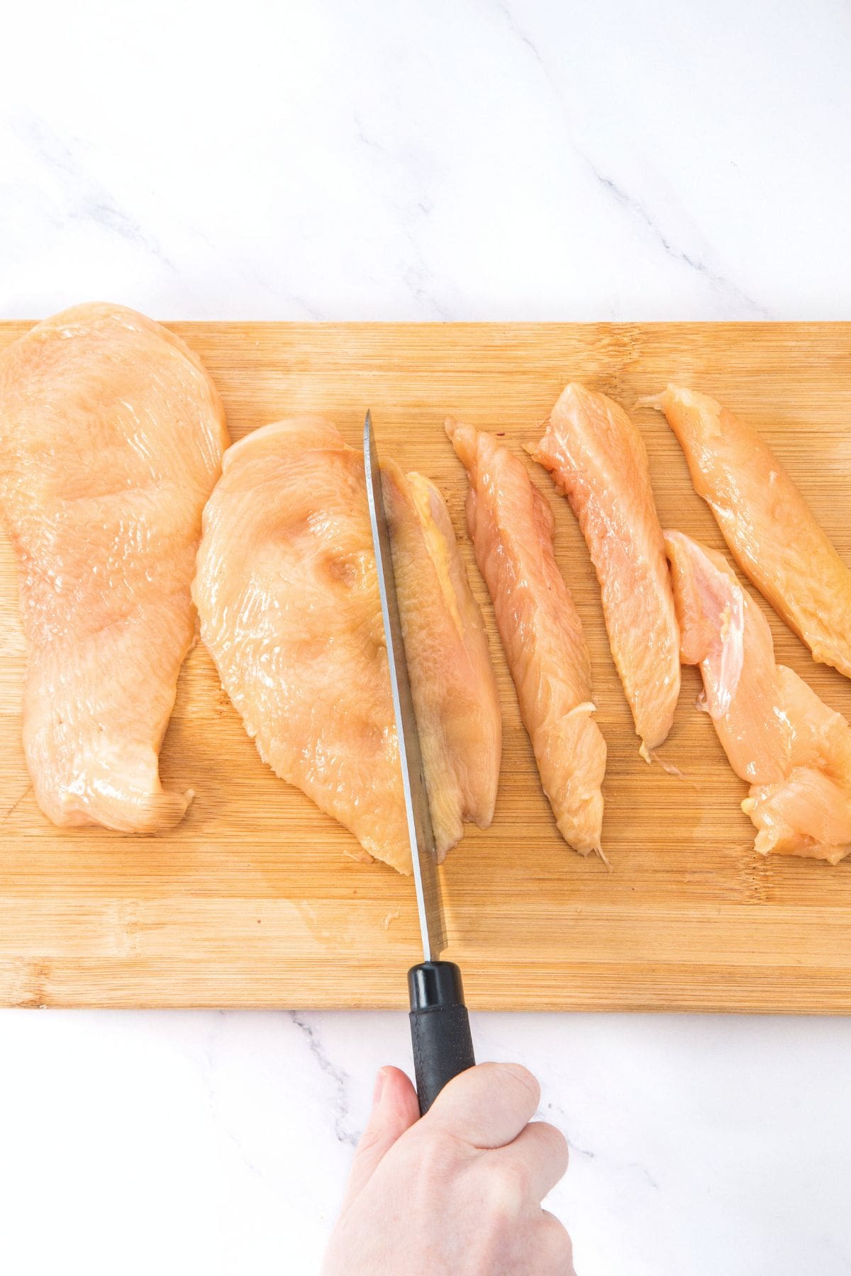 Cutting chicken breasts into strips on wooden board