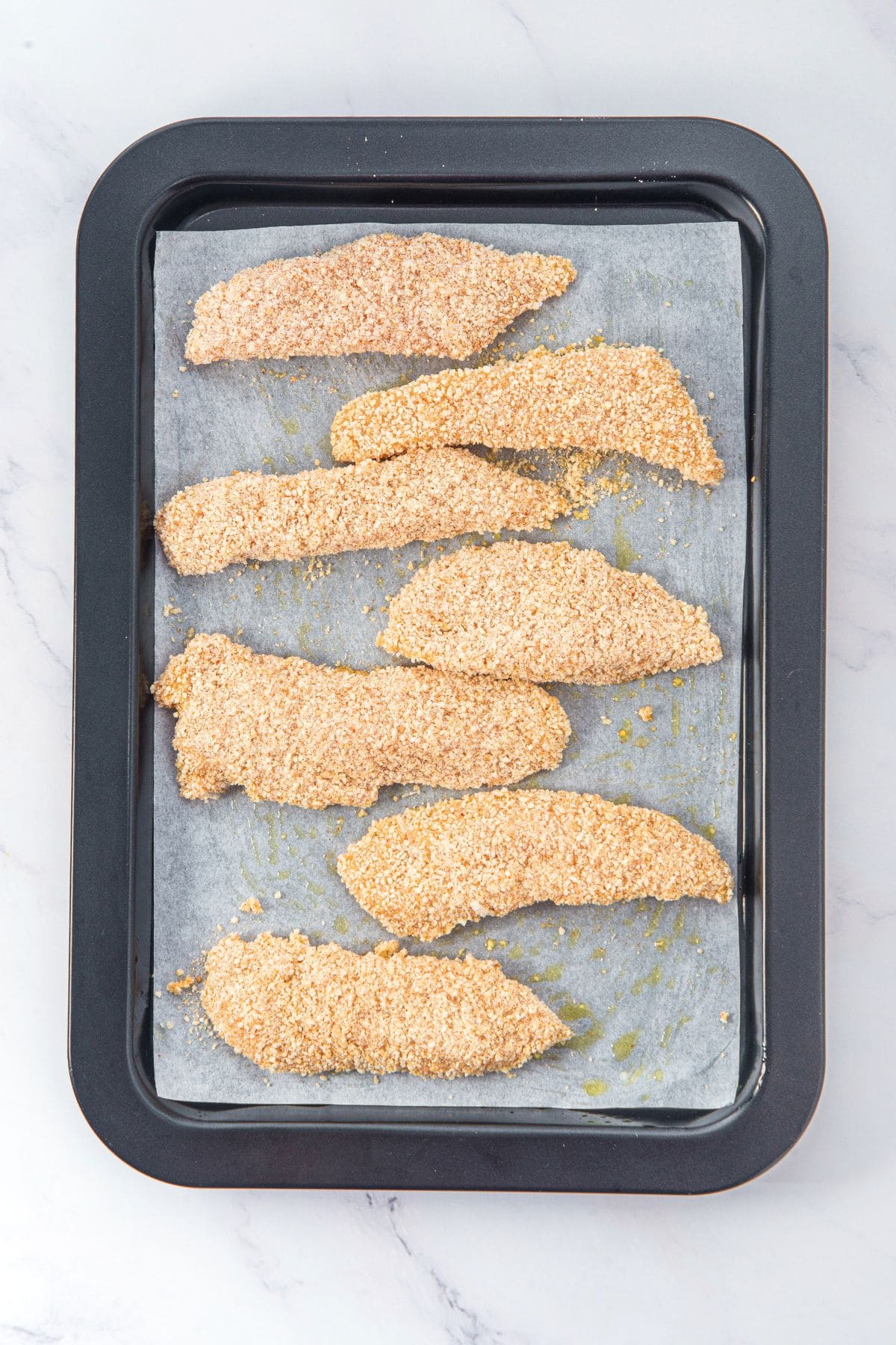 Uncooked breaded chicken tenders on parchment-lined baking sheet