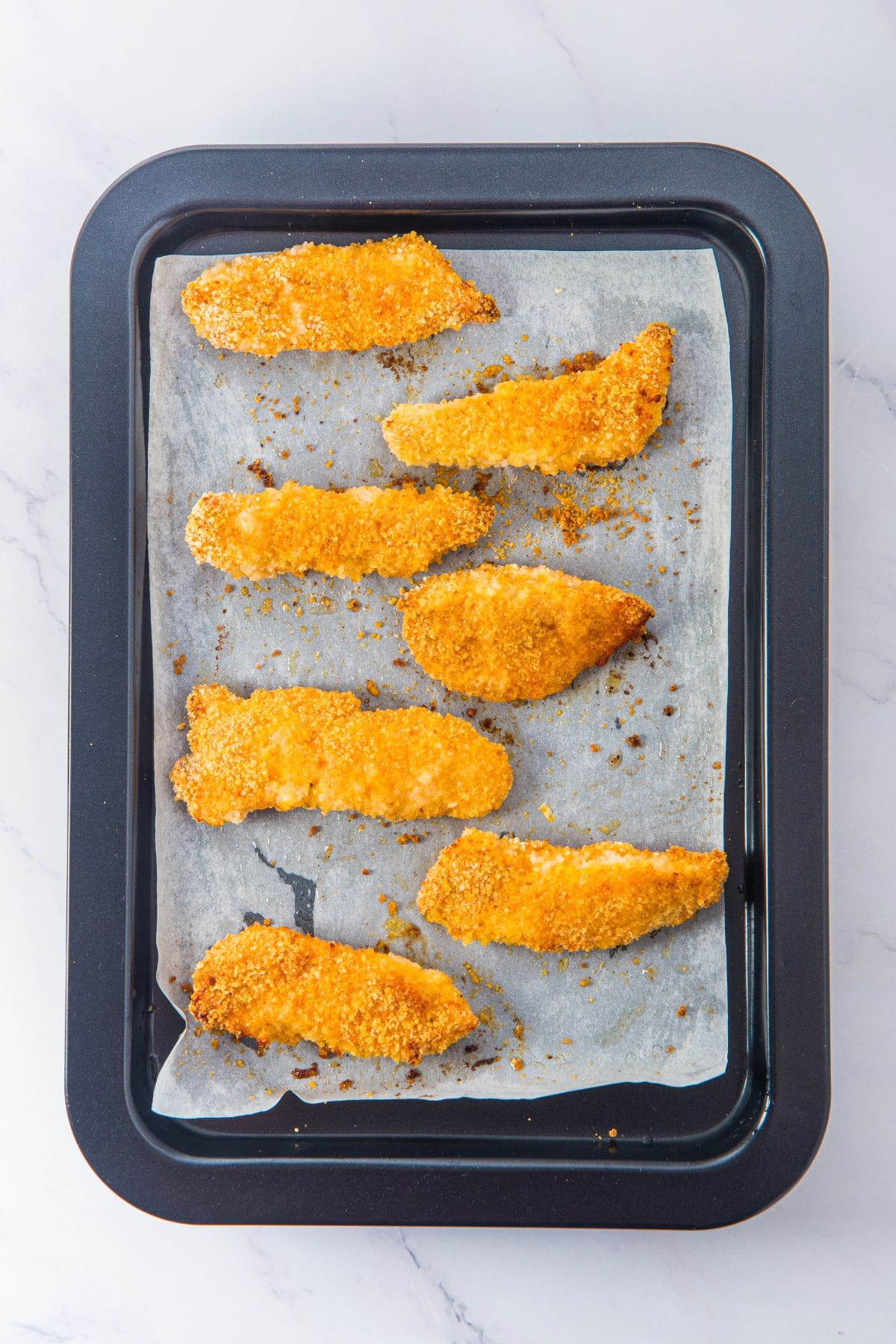 Freshly baked gluten-free chicken tenders on parchment-lined baking sheet