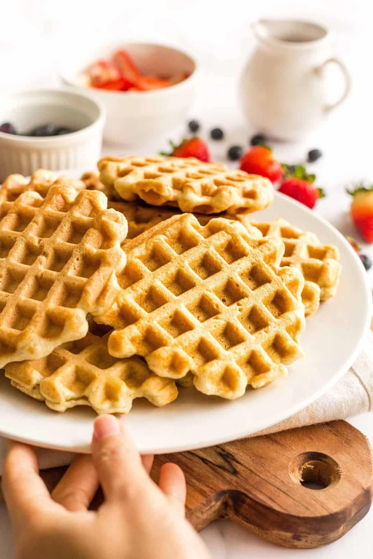 Hand reaching out for a plate of gluten-free waffles.