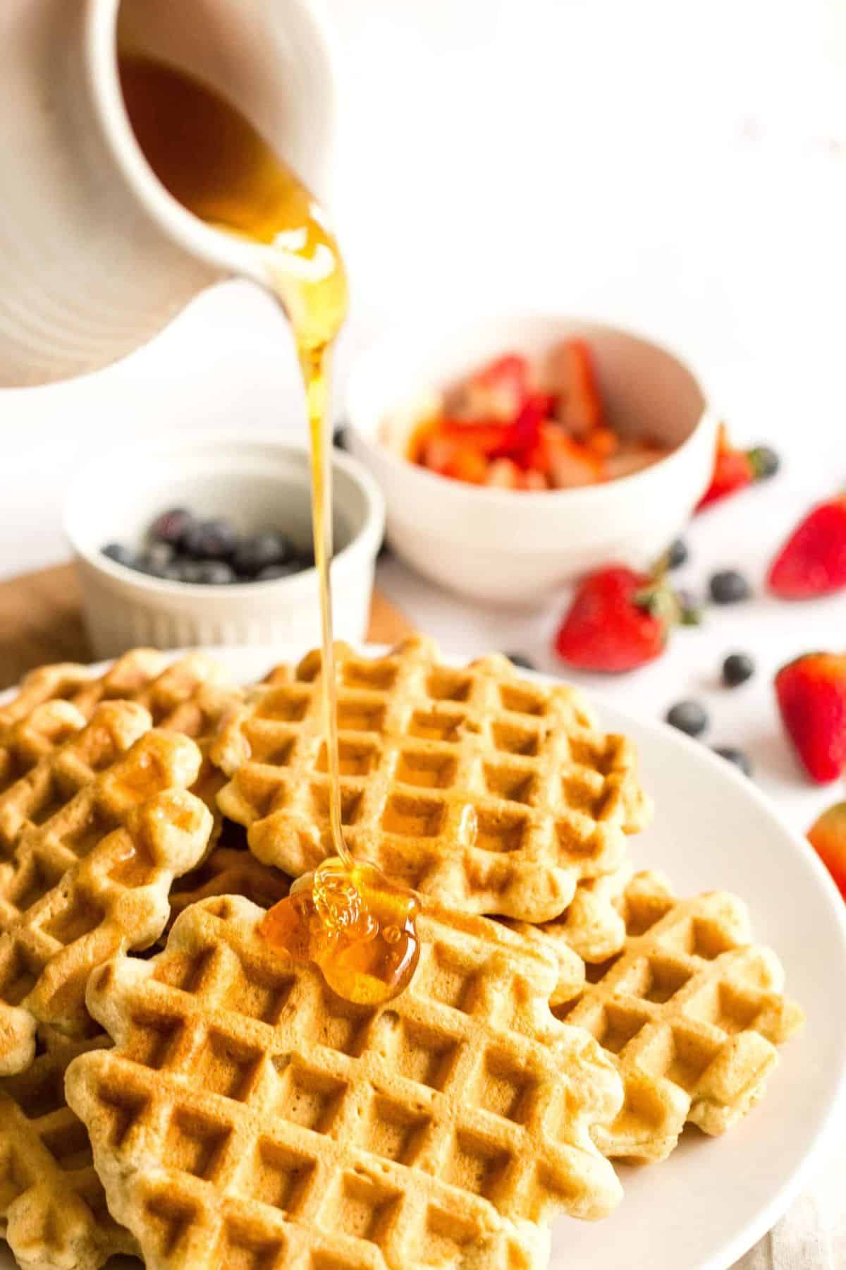 Pouring maple syrup over a plate of gluten and dairy free waffles.