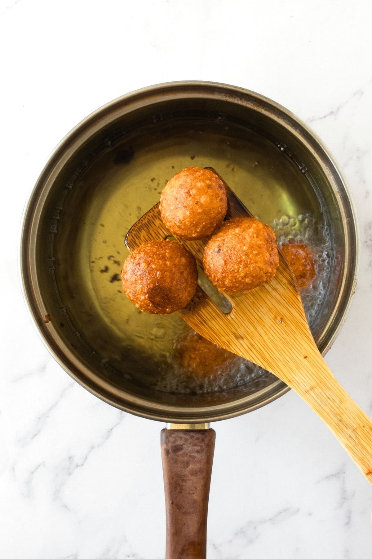 Holding up fried potato balls from a pot of oil