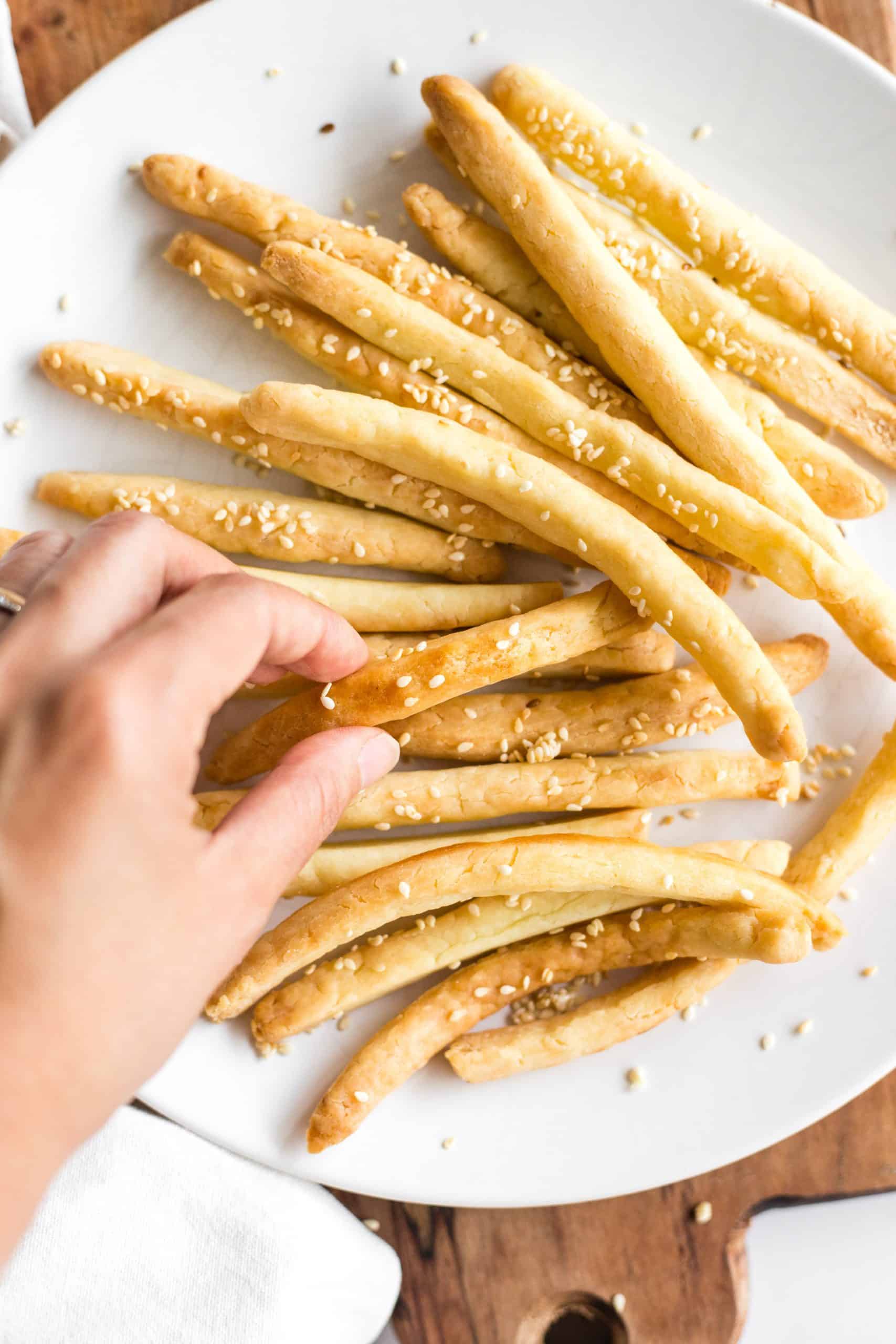 Hand reaching for a breadstick from a plate full of gluten-free grissini breadsticks.