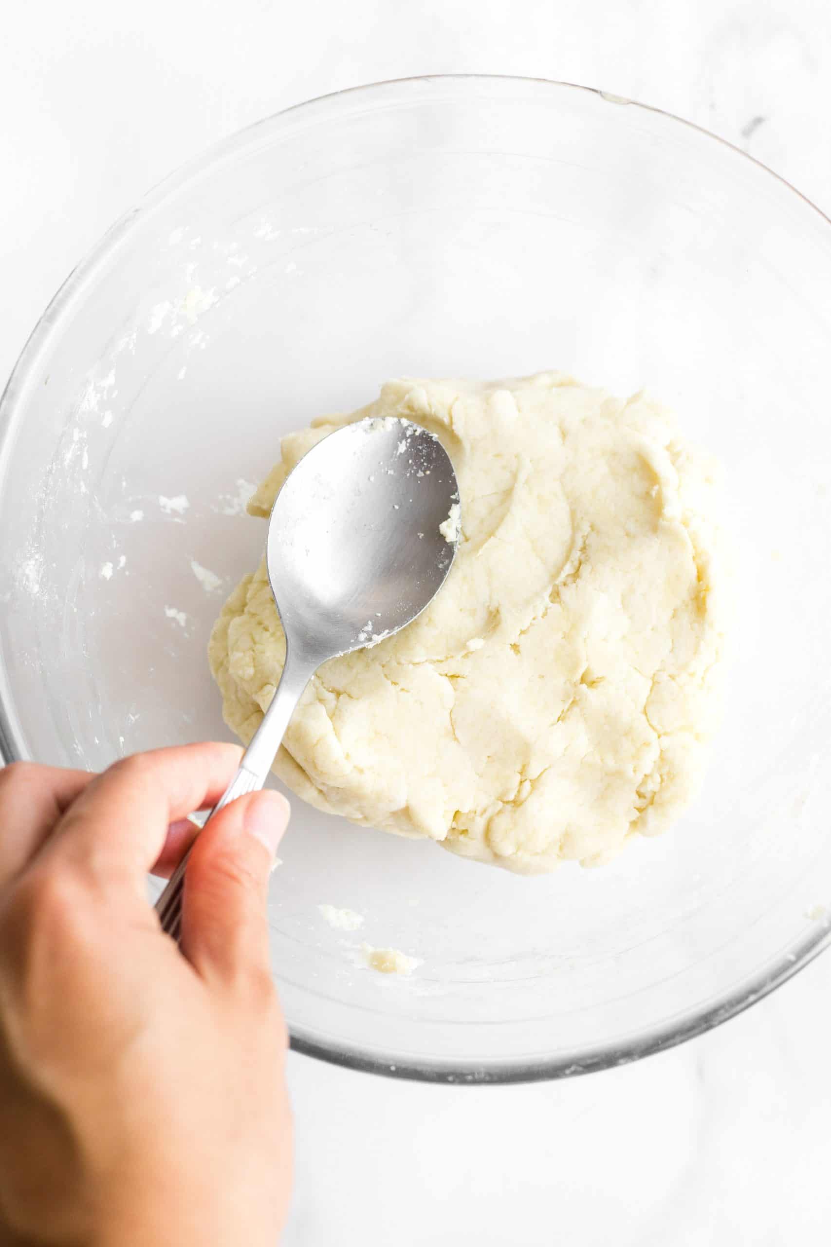 Mixing dairy-free breadsticks dough in a glass bowl with metal spoon.