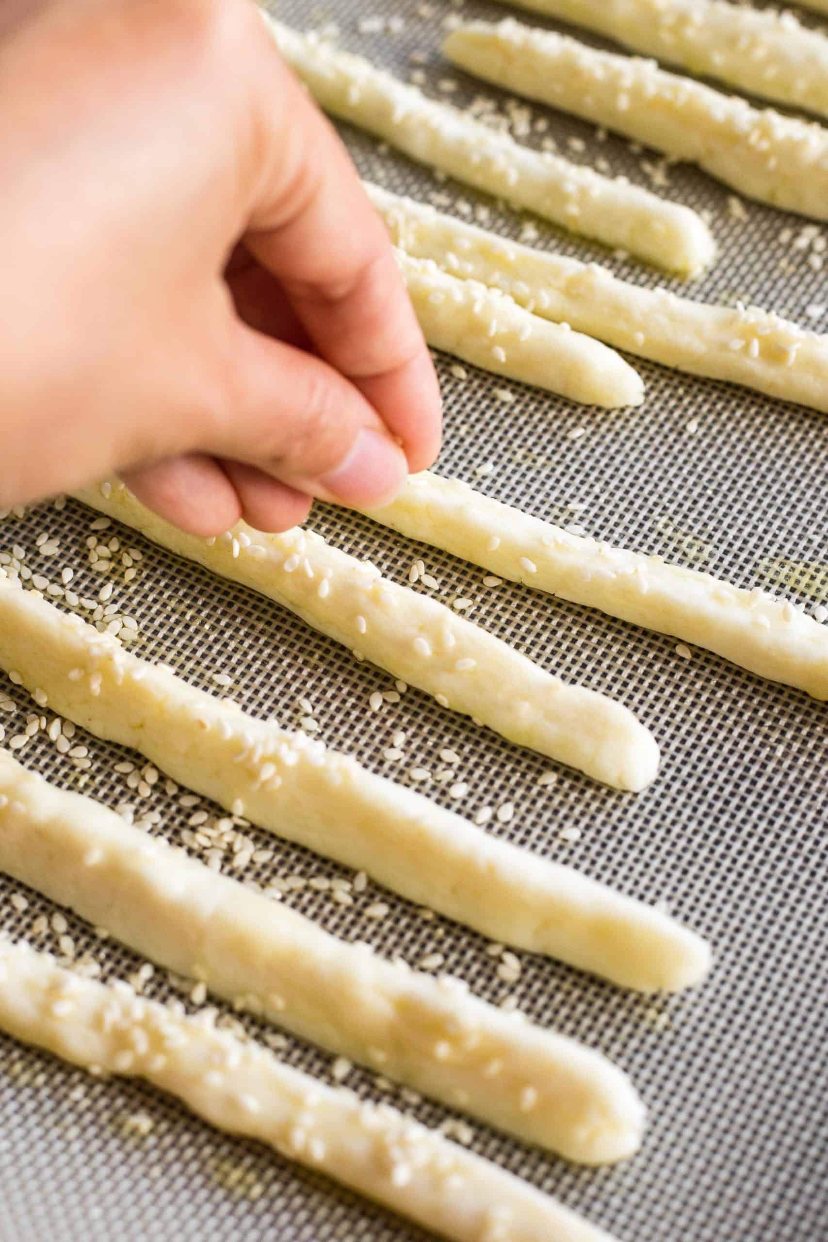 Sprinkling sesame seeds over gluten-free breadstick dough.