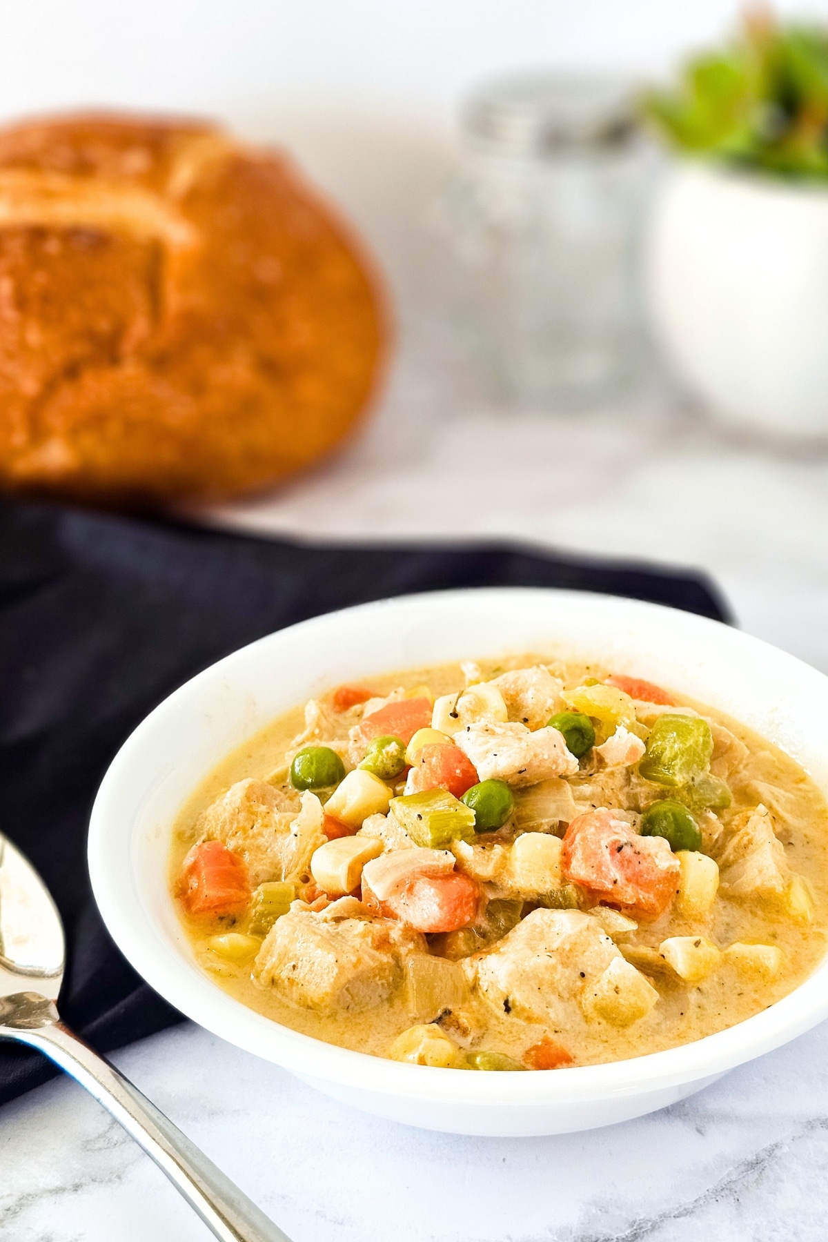 A bowl of chicken pie soup and spoon on marble board.