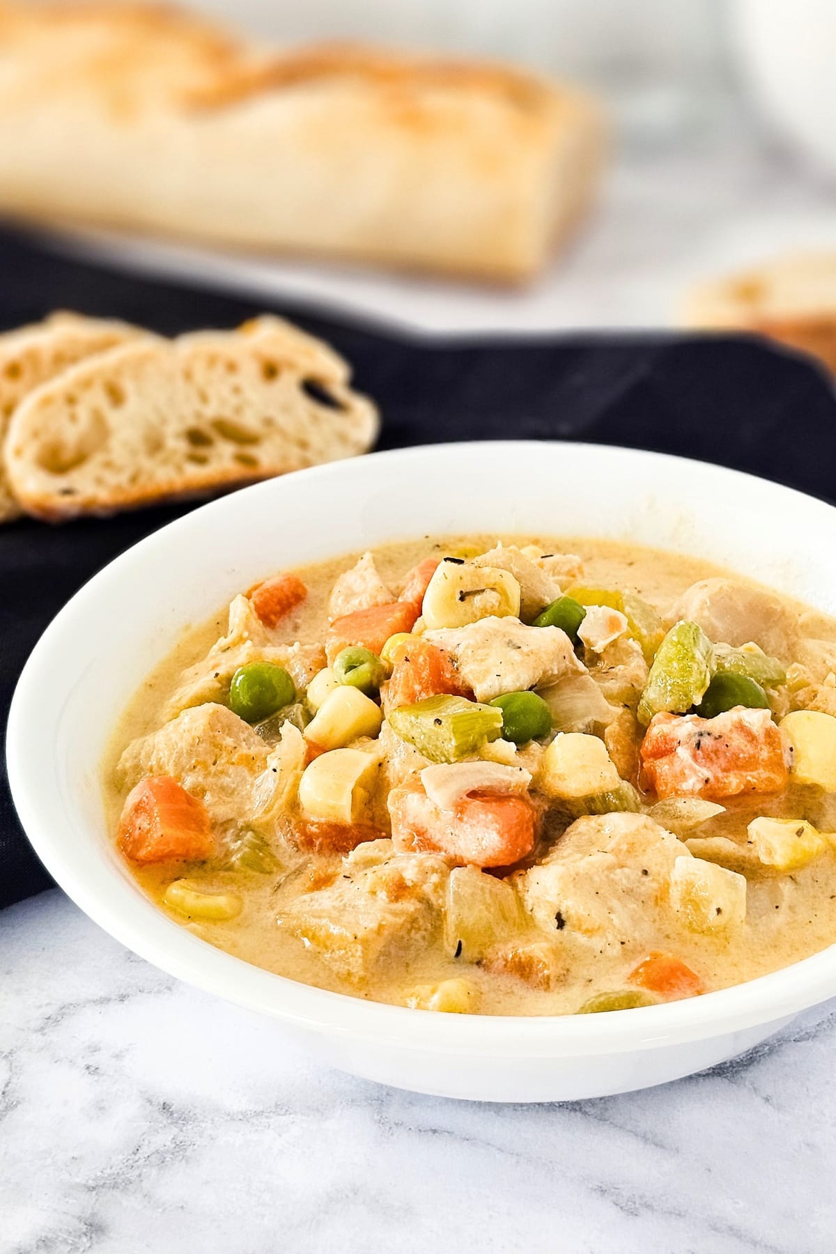 A bowl of chicken pot pie soup on marble board.