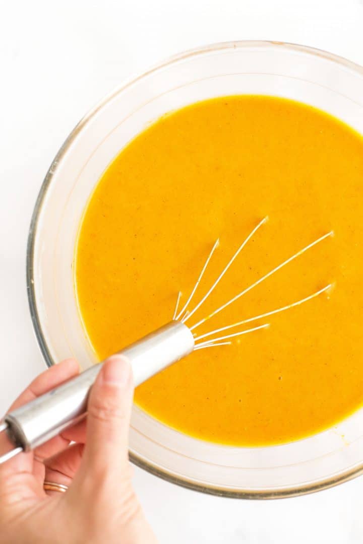 Whisking orange liquid mixture in glass mixing bowl.