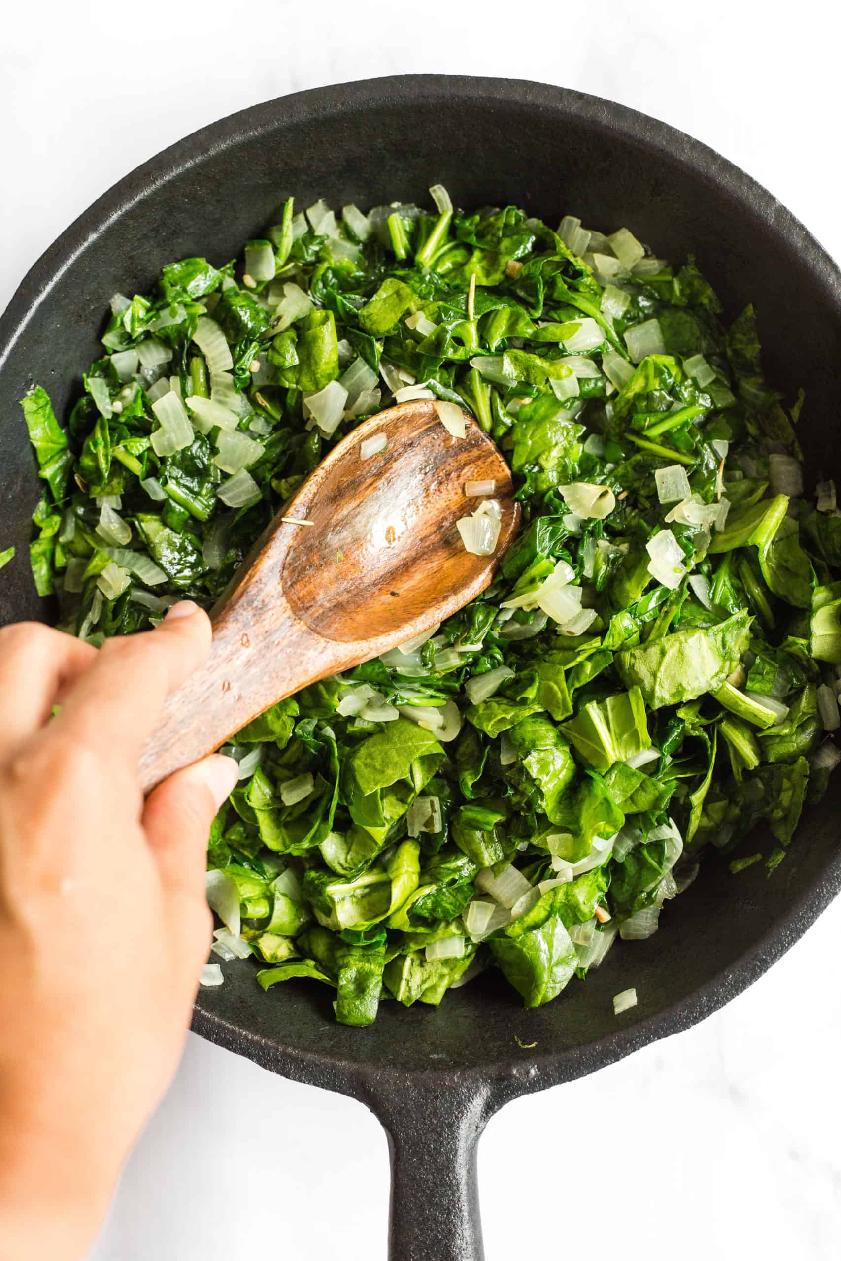 Sautéing onions and spinach in a cast iron skillet.